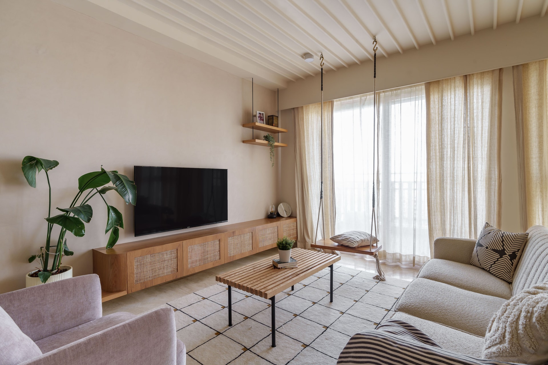 Neutral-toned living room with wood tv console, hanging swing, and sheer curtains lit by daylight