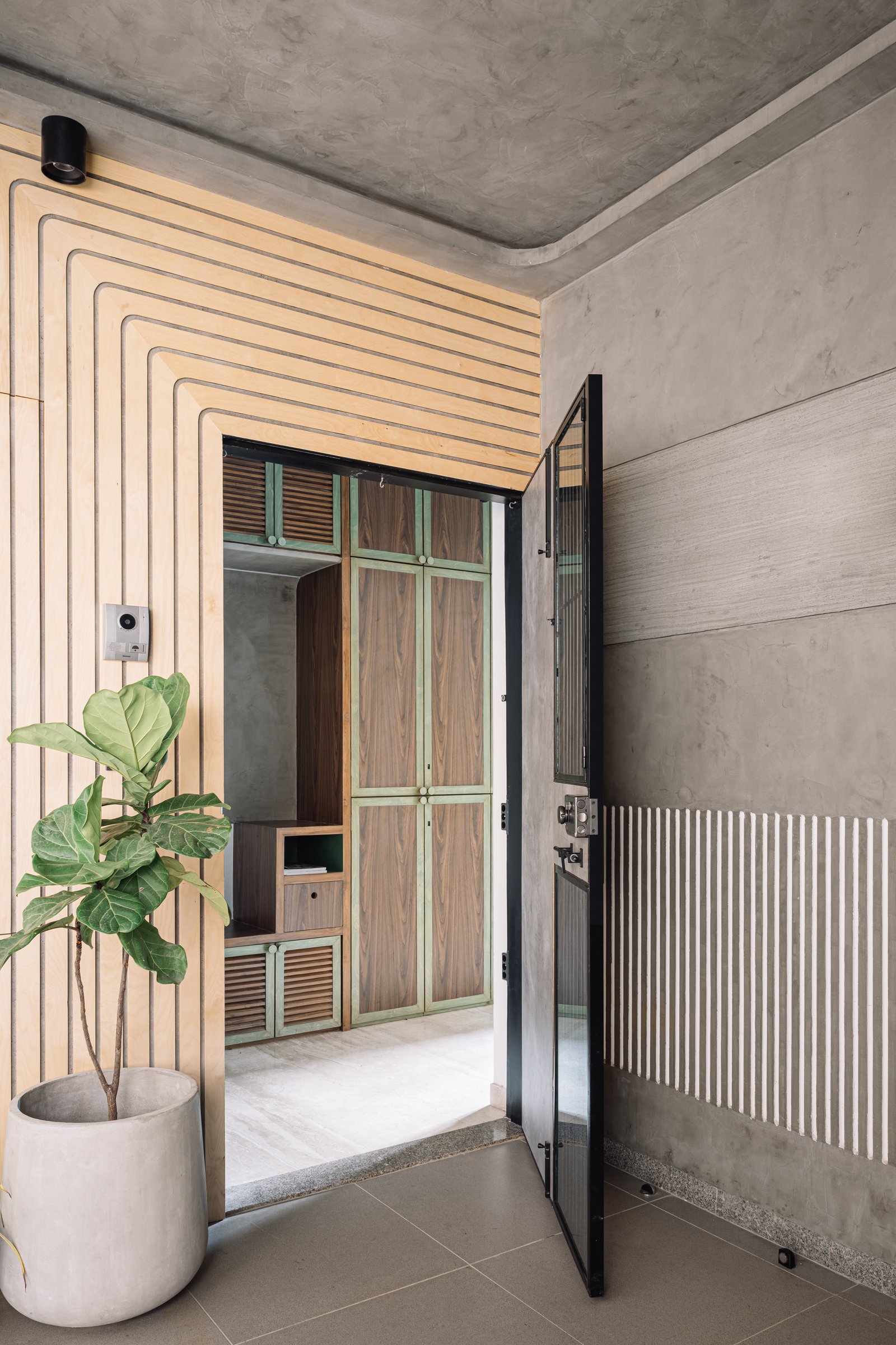 The entry threshold, where routed timber grooves curve overhead to meet the concrete ceiling beyond