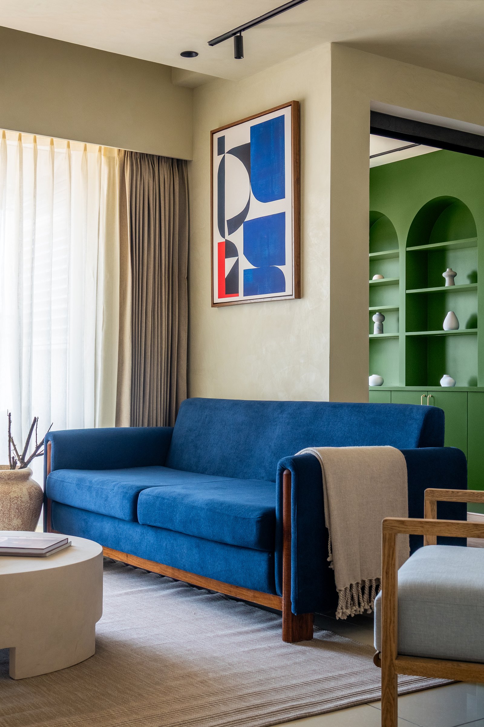 The living room: a cobalt velvet sofa and arched green shelving unit establish the home's chromatic argument from the first glance