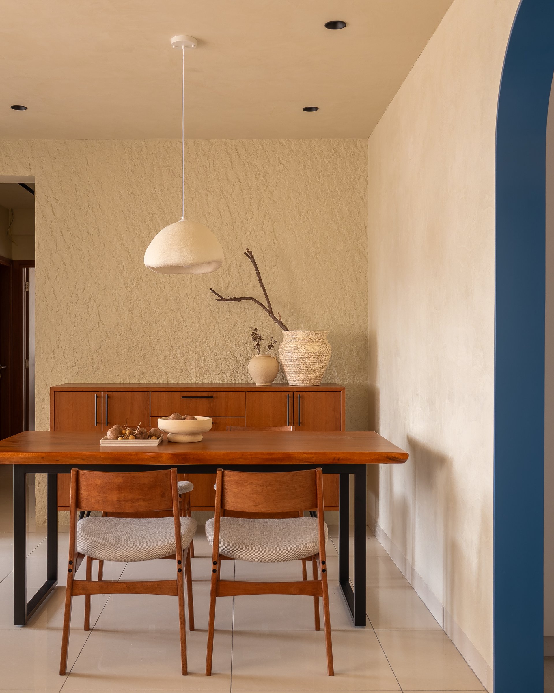 The dining nook in quieter light: the textured feature wall deepens, and the warm timber sideboard holds just enough