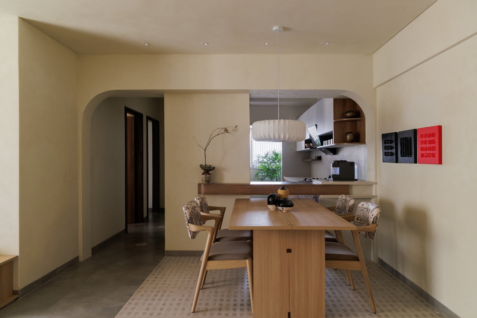 The dining area, where a soft arch frames the kitchen pass-through and a paper-lantern pendant softens the geometry