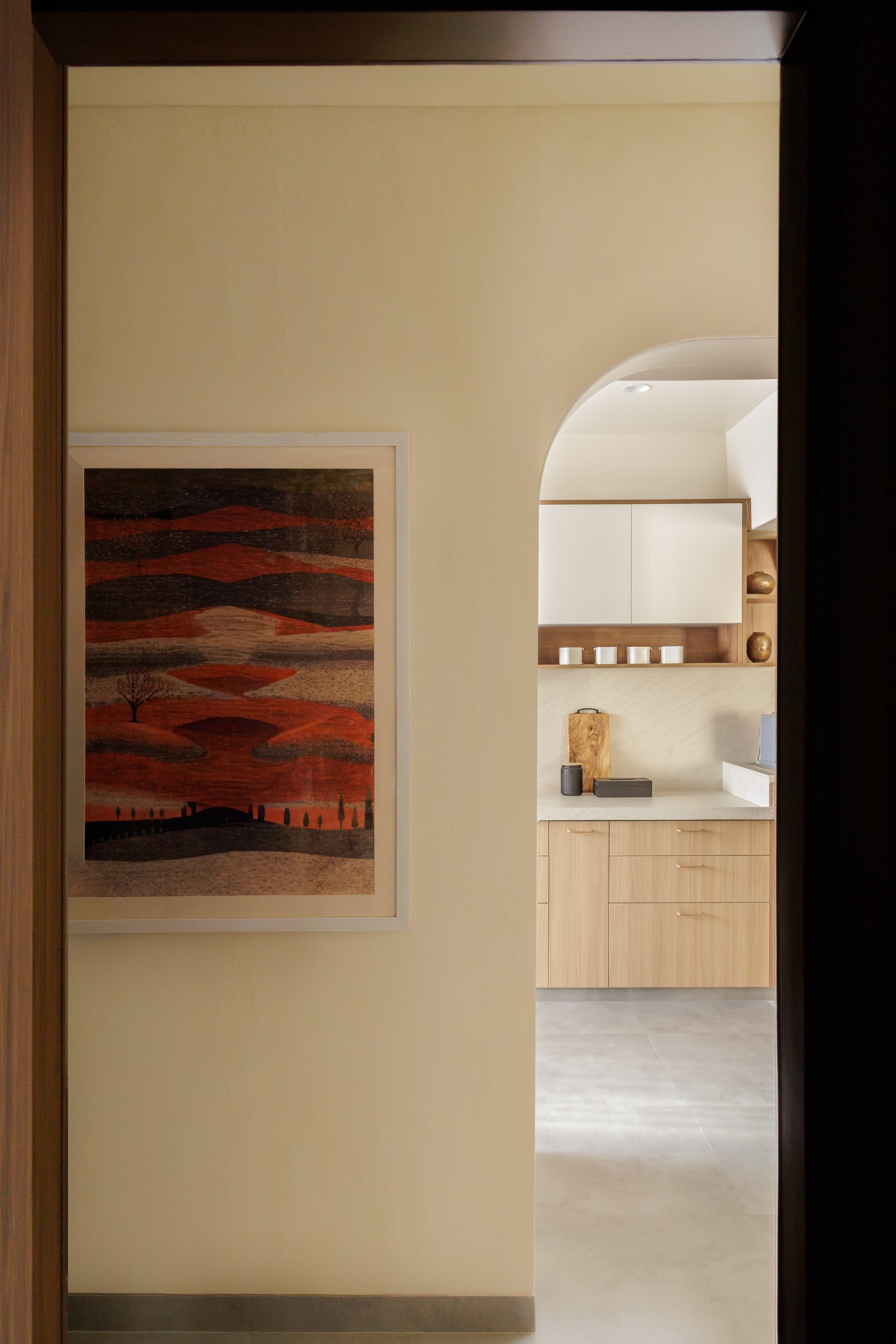 A passage framed by an arched opening, where a single landscape painting becomes a hinge between zones