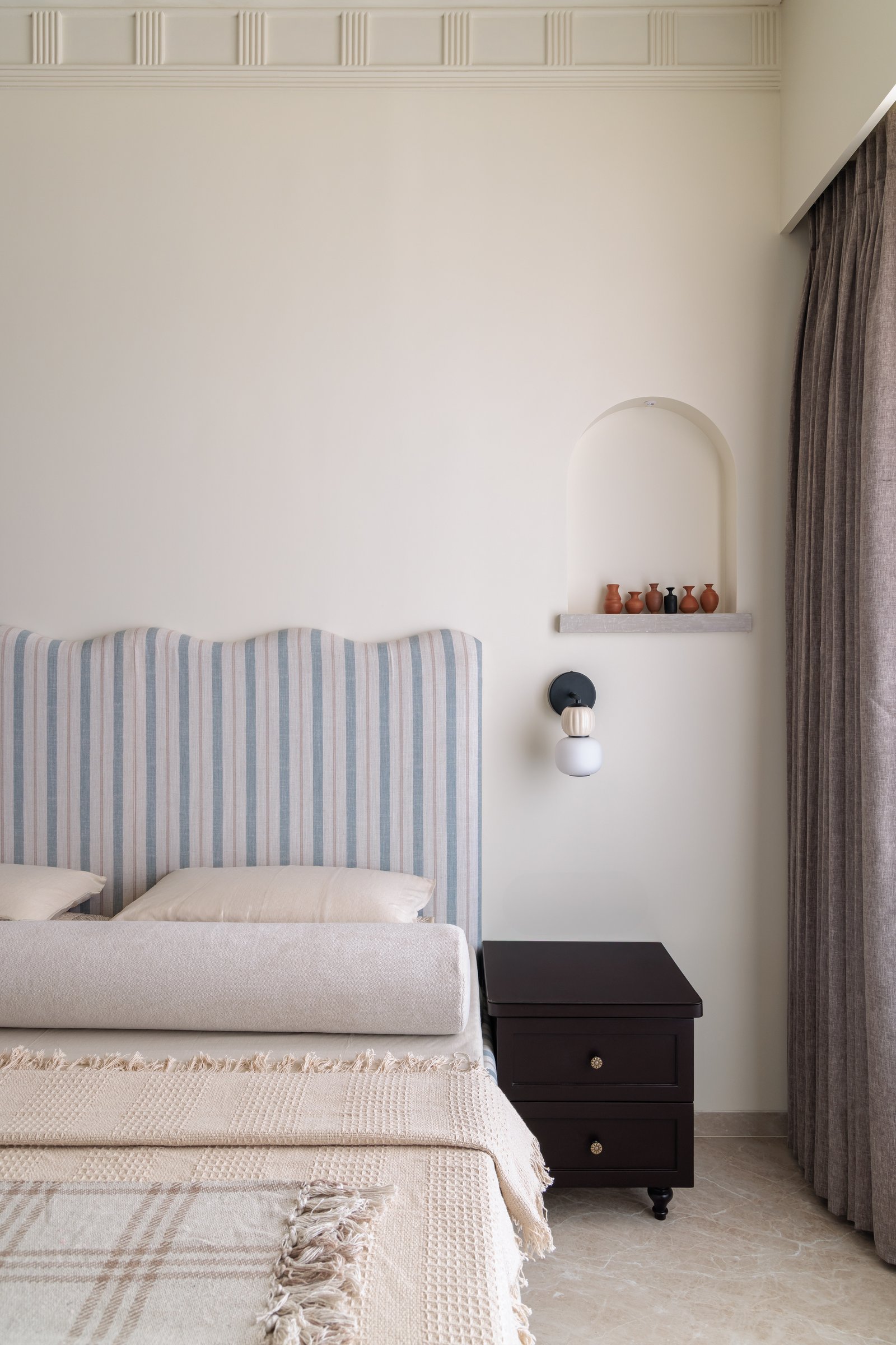 Bedside detail in the second bedroom: an arched niche with miniature terracotta vessels and a compact wall sconce