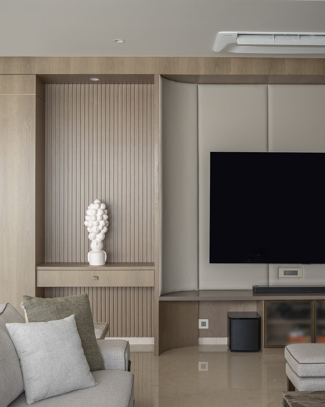The living room's television wall, where a curved upholstered panel and fluted timber niches absorb the screen into the architecture
