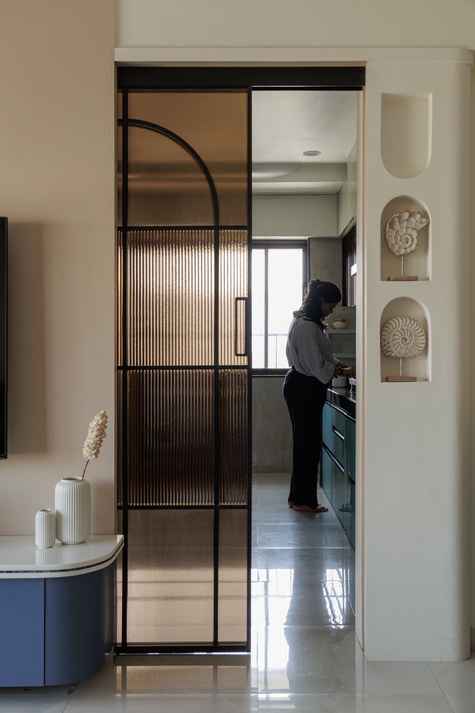 Looking back from the living room into the kitchen, the reeded glass door framing the service zone as a luminous chamber