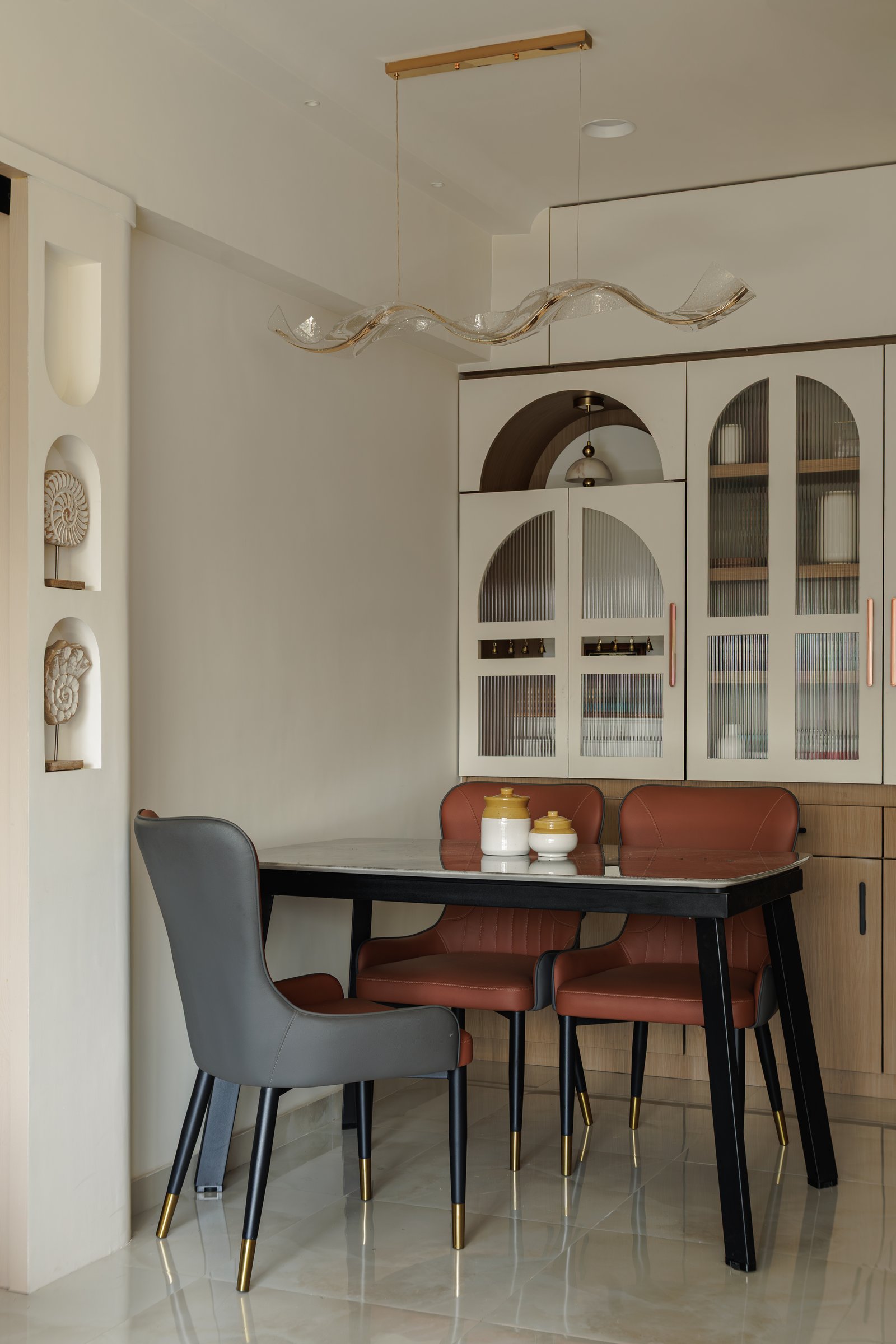 The dining nook with its arched fluted-glass display unit and mixed upholstered seating, the tropical retreat reference held in tone rather than ornament