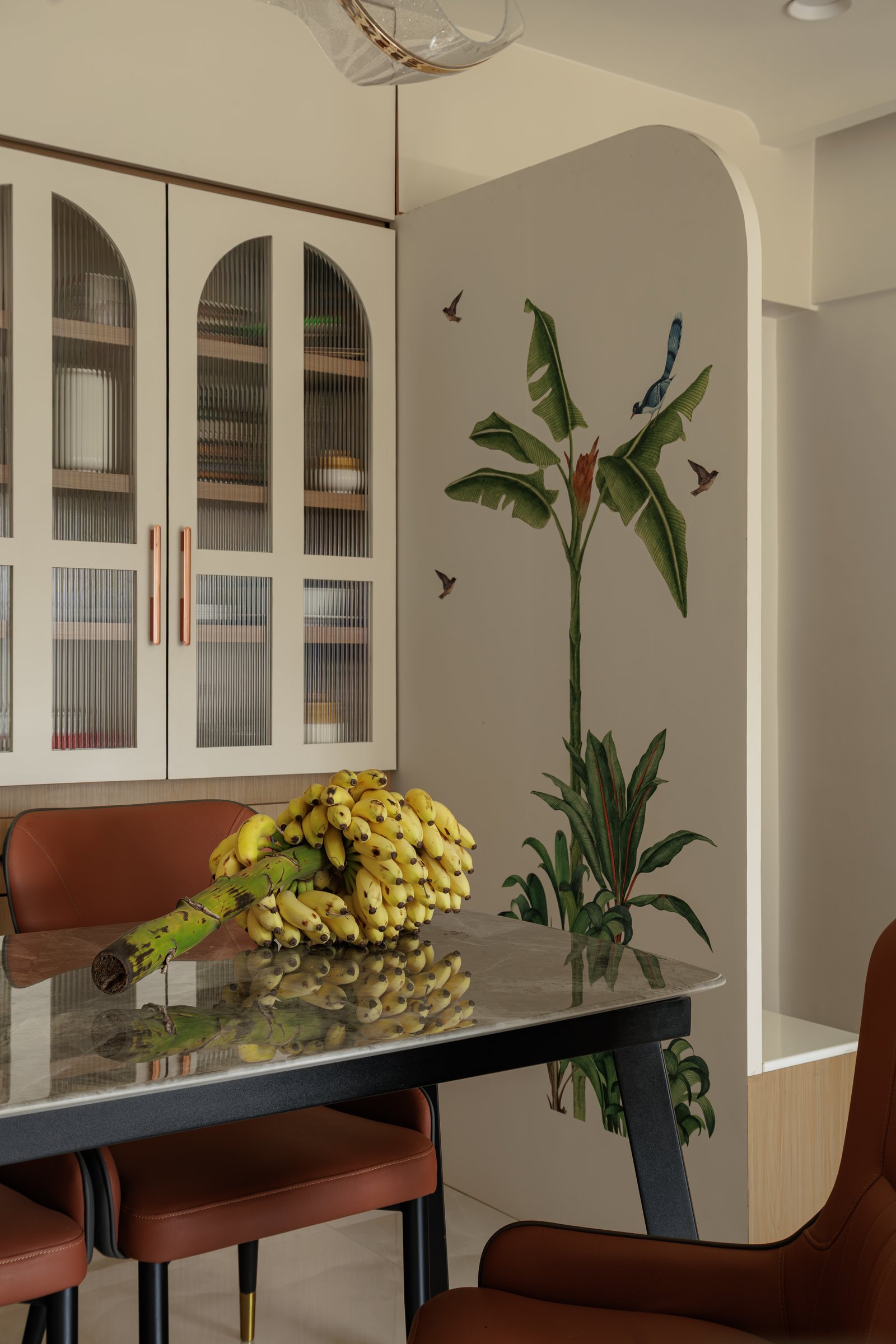 A hand-painted banana plant and birds unfurl beside the dining cabinetry, the source of the nook's tropical theme
