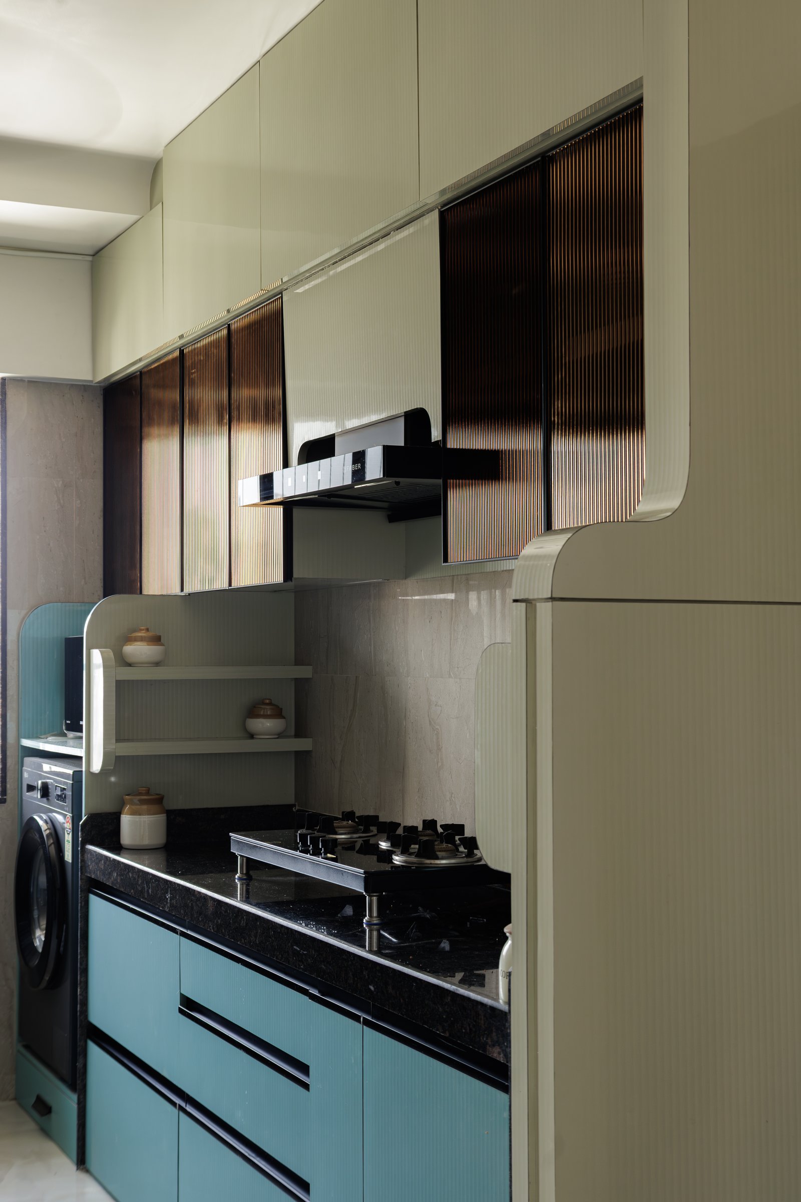 The galley kitchen in muted sage and dusky teal, with fluted bronze-tinted glass softening the upper cabinetry