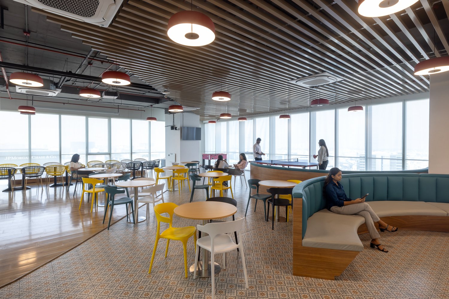 The cafeteria: patterned cement tile, a slatted wood ceiling, and red pendant shades shift the tonal register from the workstation floor