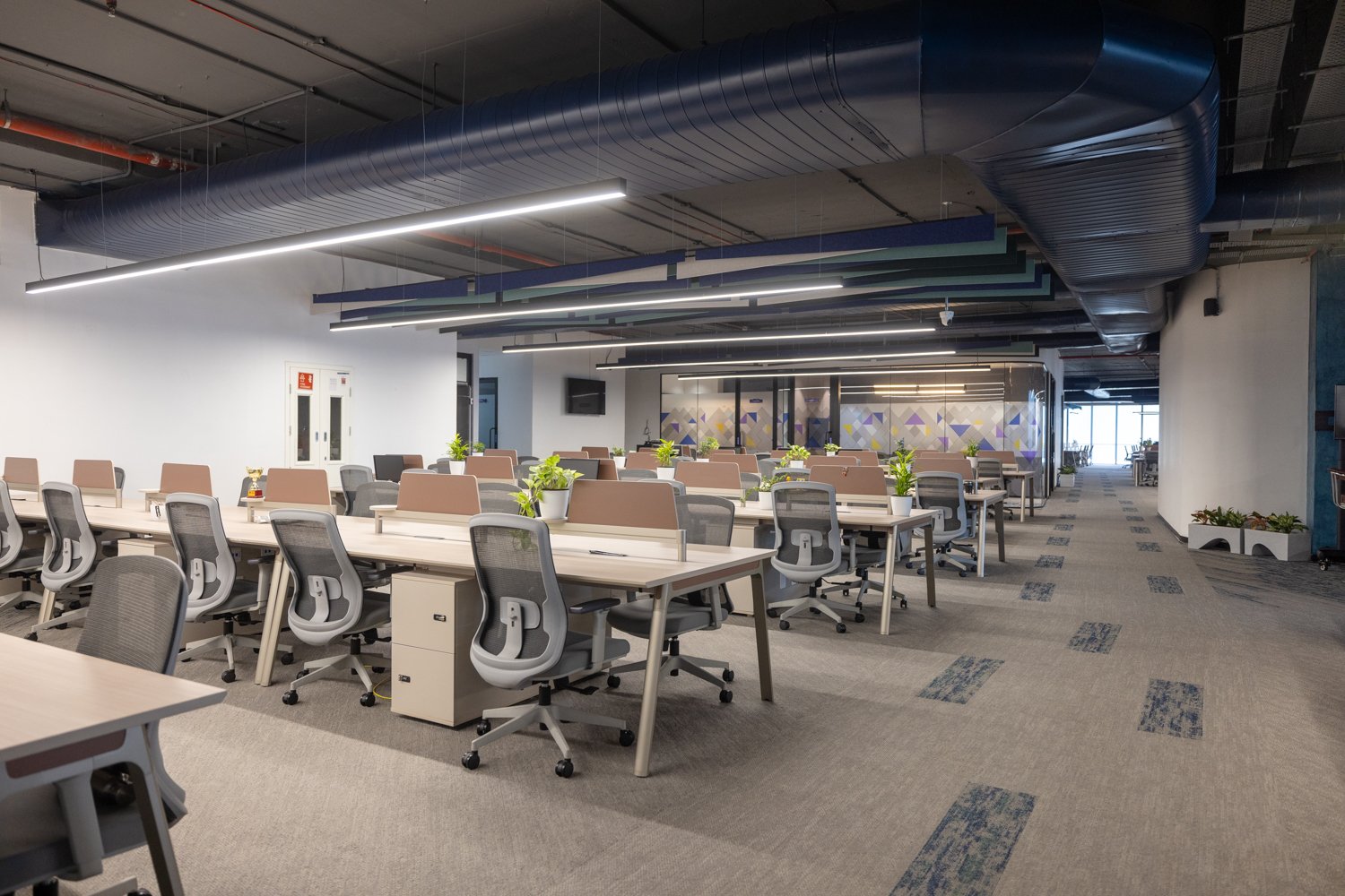 The open workstation zone, where suspended acoustic baffles in layered blues and greens give the ceiling its rhythm