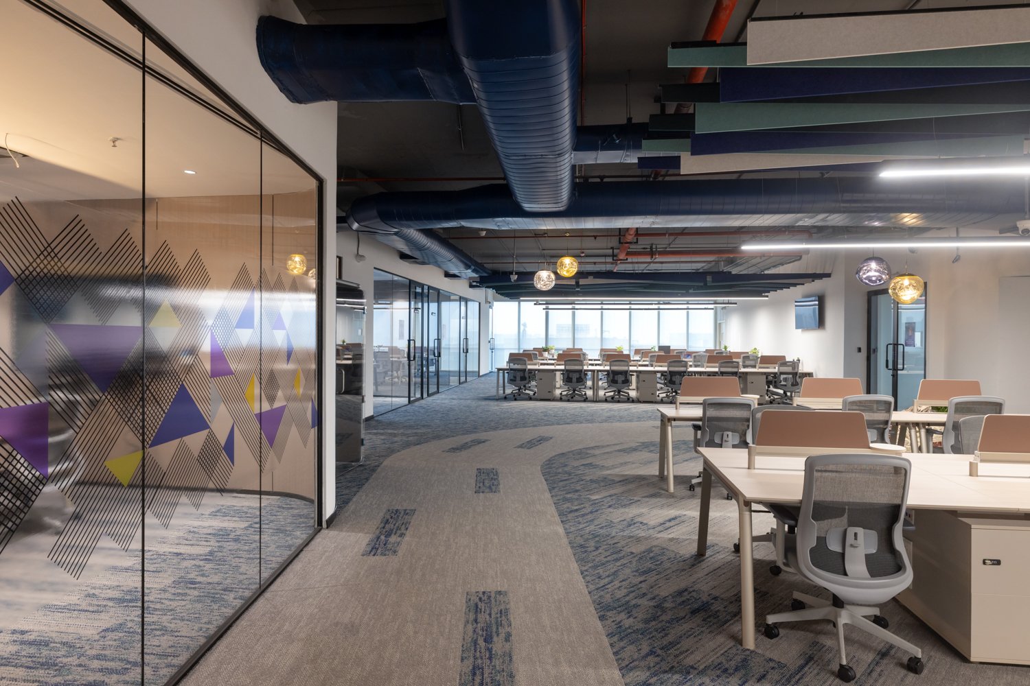 Circulation along the floor's spine, where amber glass pendants and the studio's signature patterned partition mark the principal path