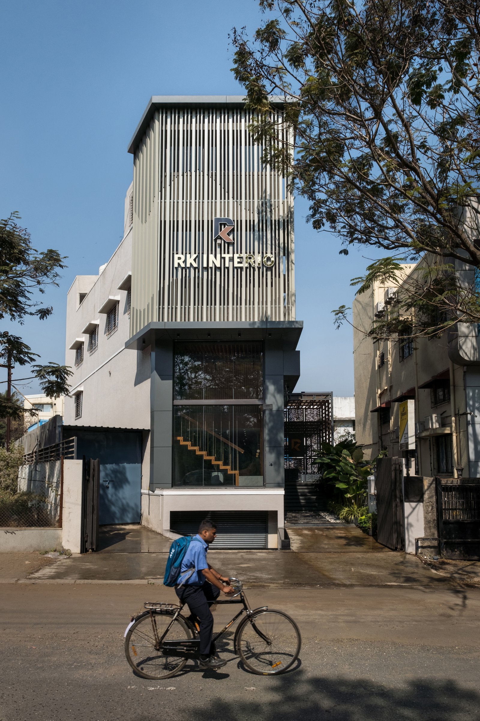 The street elevation: a composed vertical volume crowned by metal louvers, with the double-height glazed frontage opening the ground level to the public realm