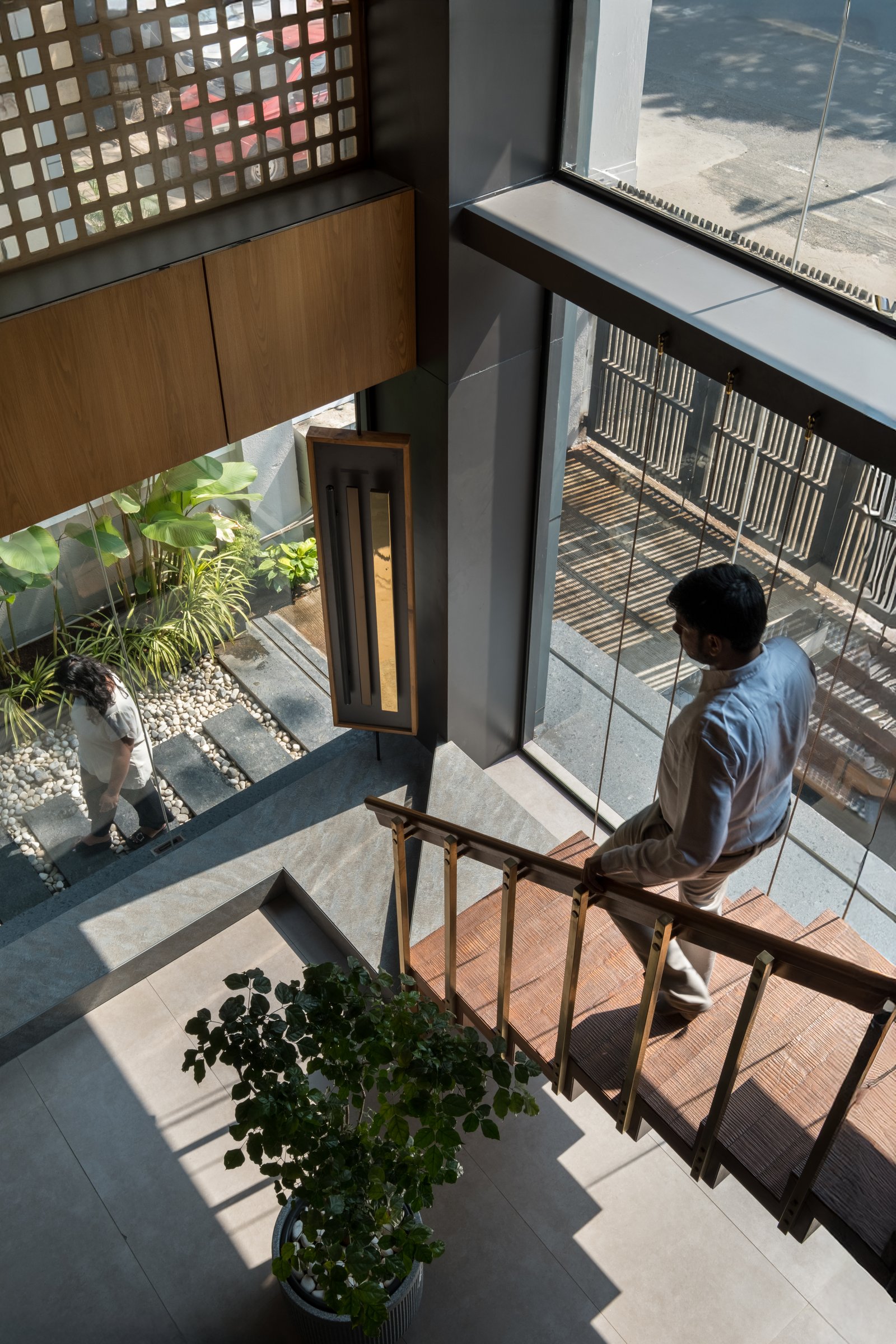 The staircase descends past the double-height glazing, holding the pebble-bed entry garden and the interior in one continuous glance