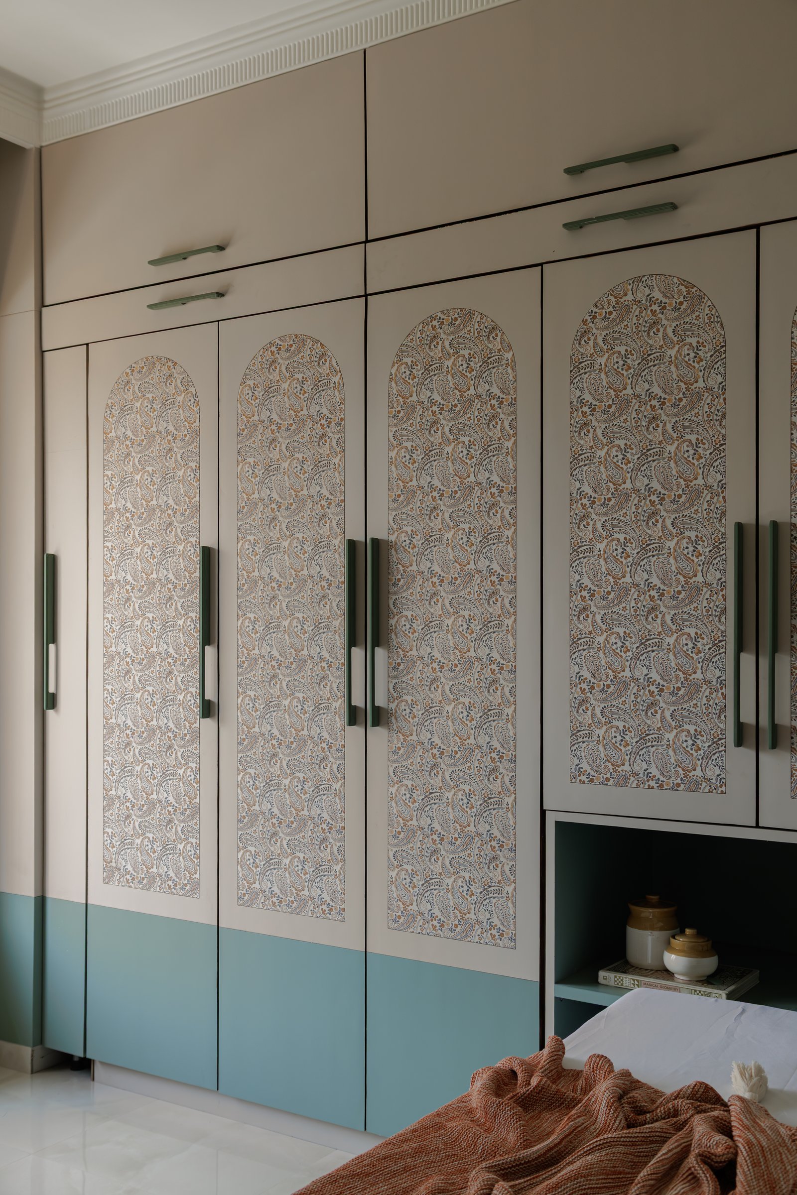 The master wardrobe wall: paisley-printed arched panels banded with dusty teal, a contemporary reading of block-printed textile language