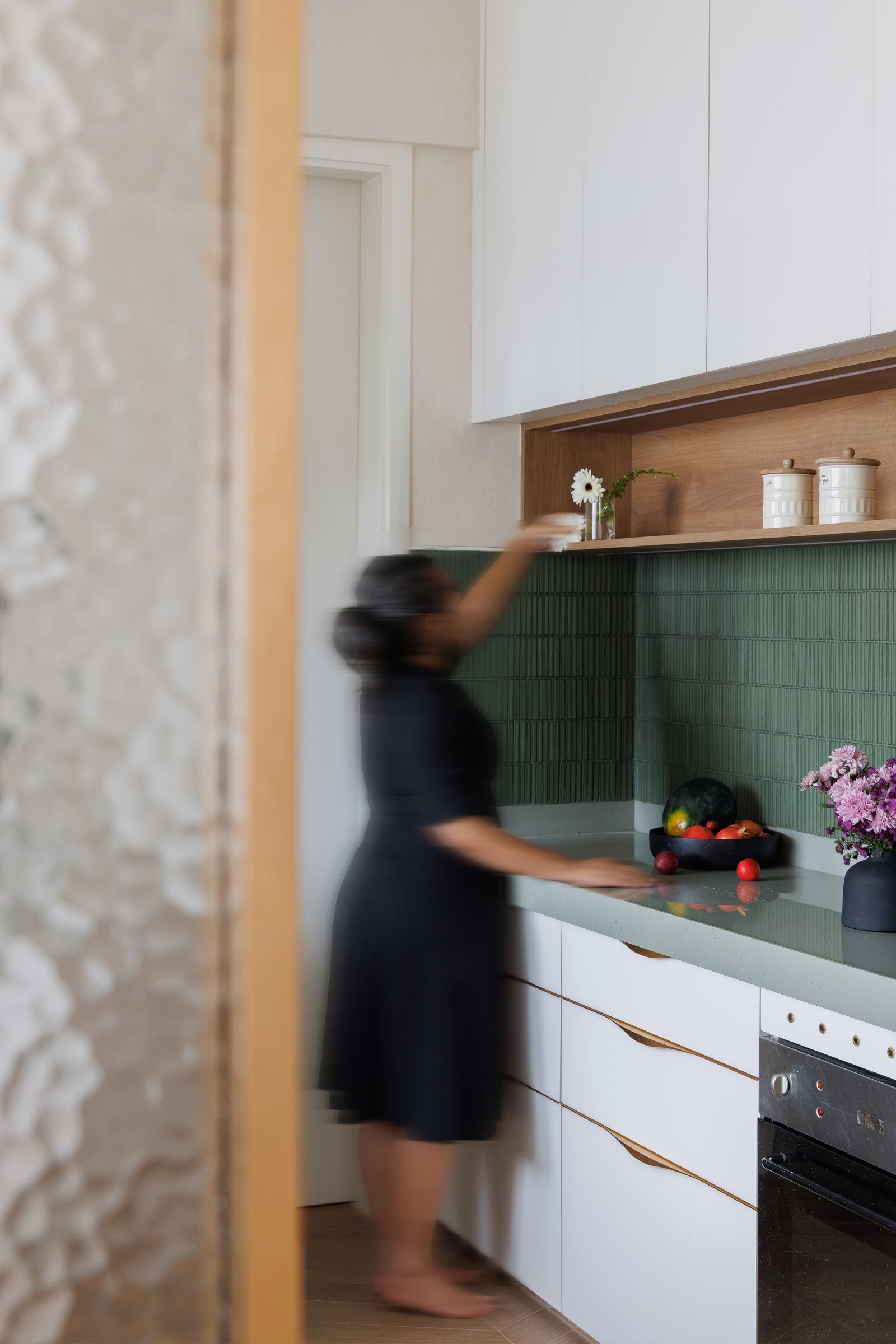 Inside the kitchen, crisp white cabinetry meets a sage tile backsplash in narrow vertical format