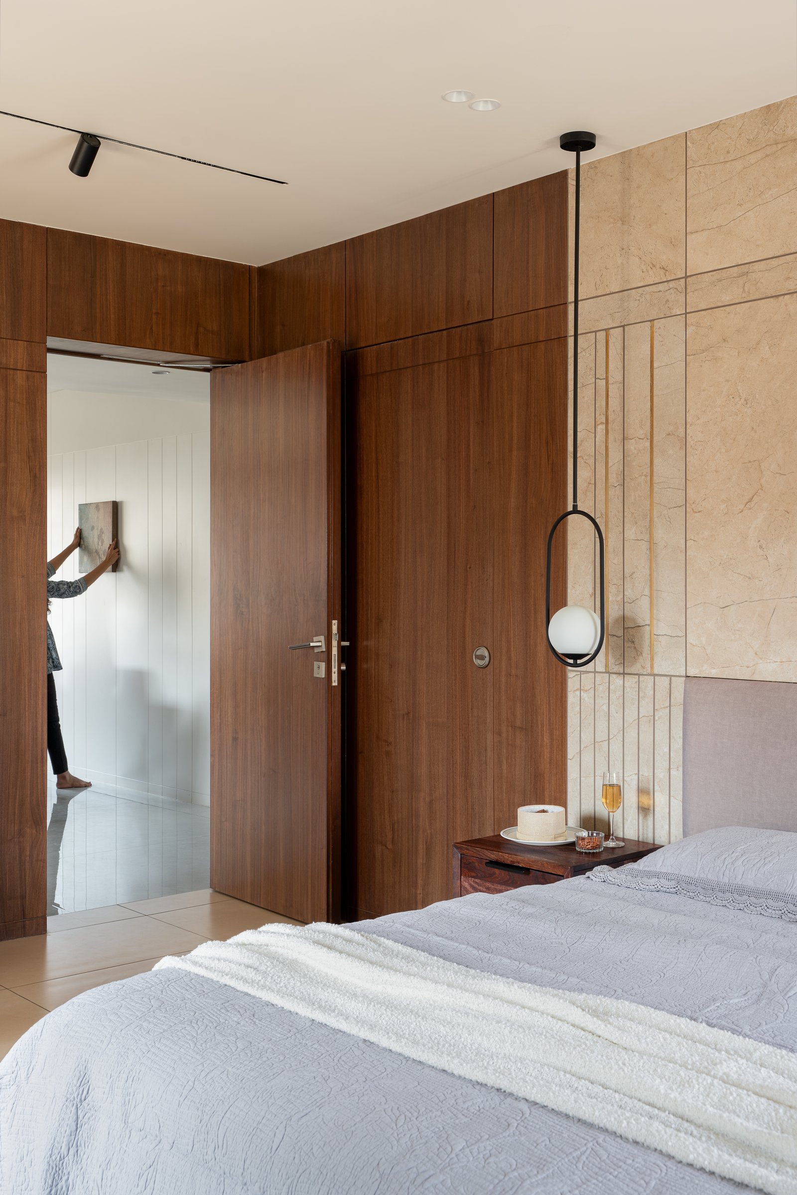 The guest bedroom, where a travertine panel inlaid with brass lines meets a muted lilac headboard