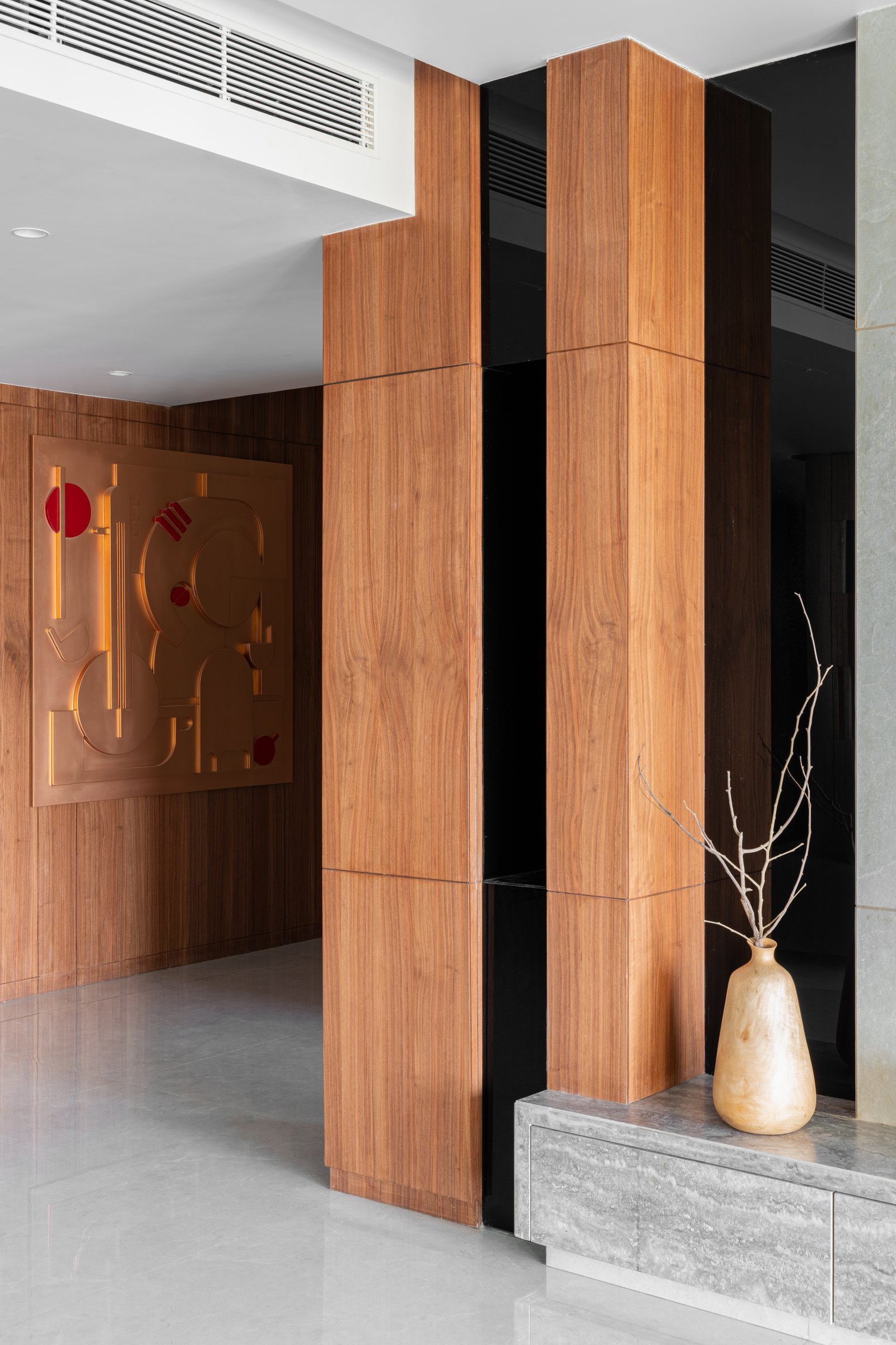 The entry foyer, where walnut panelling and a copper-toned Ganpati artwork establish the material grammar