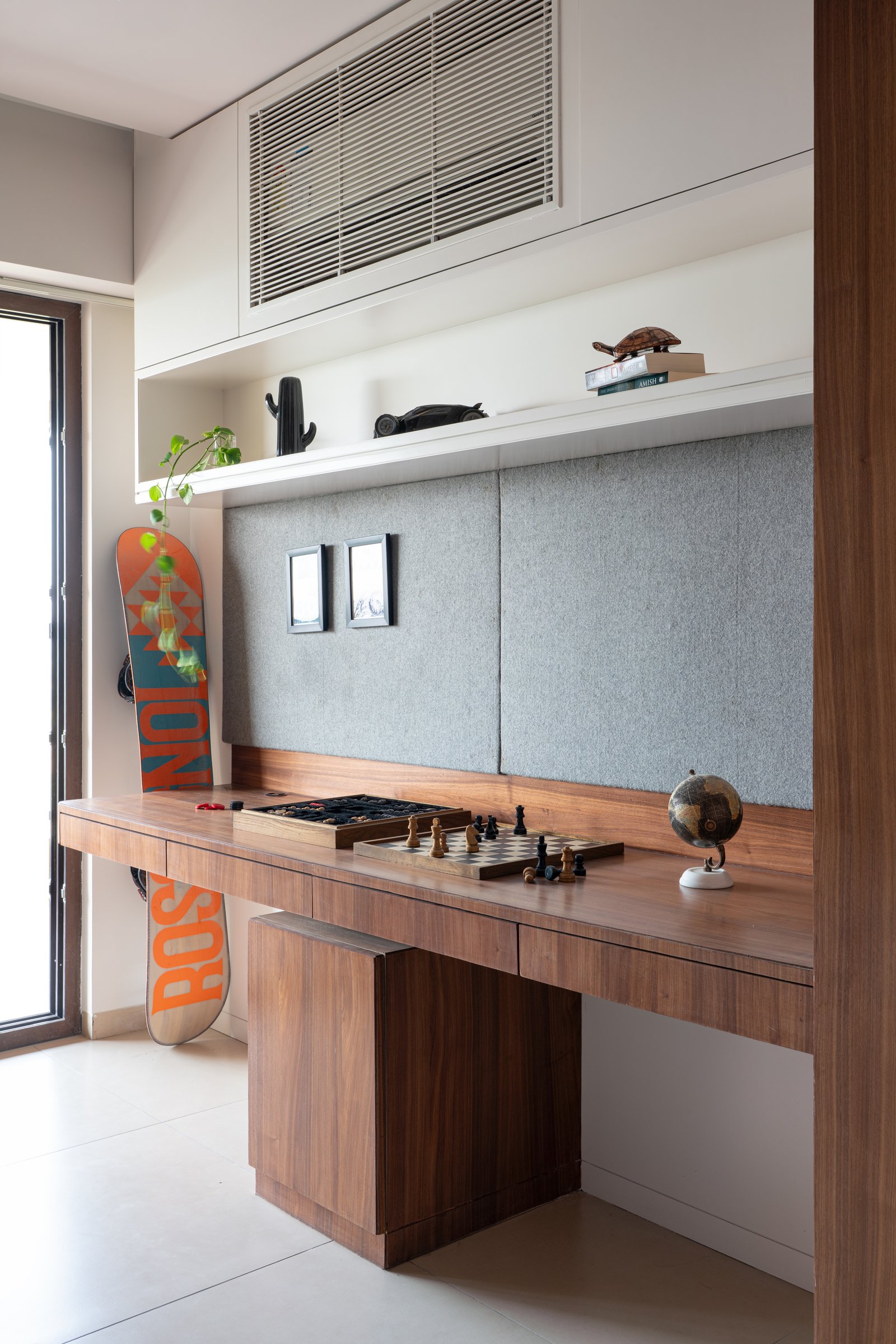A second, informal study nook within a bedroom holds a long walnut desk beneath a felt-upholstered pinboard