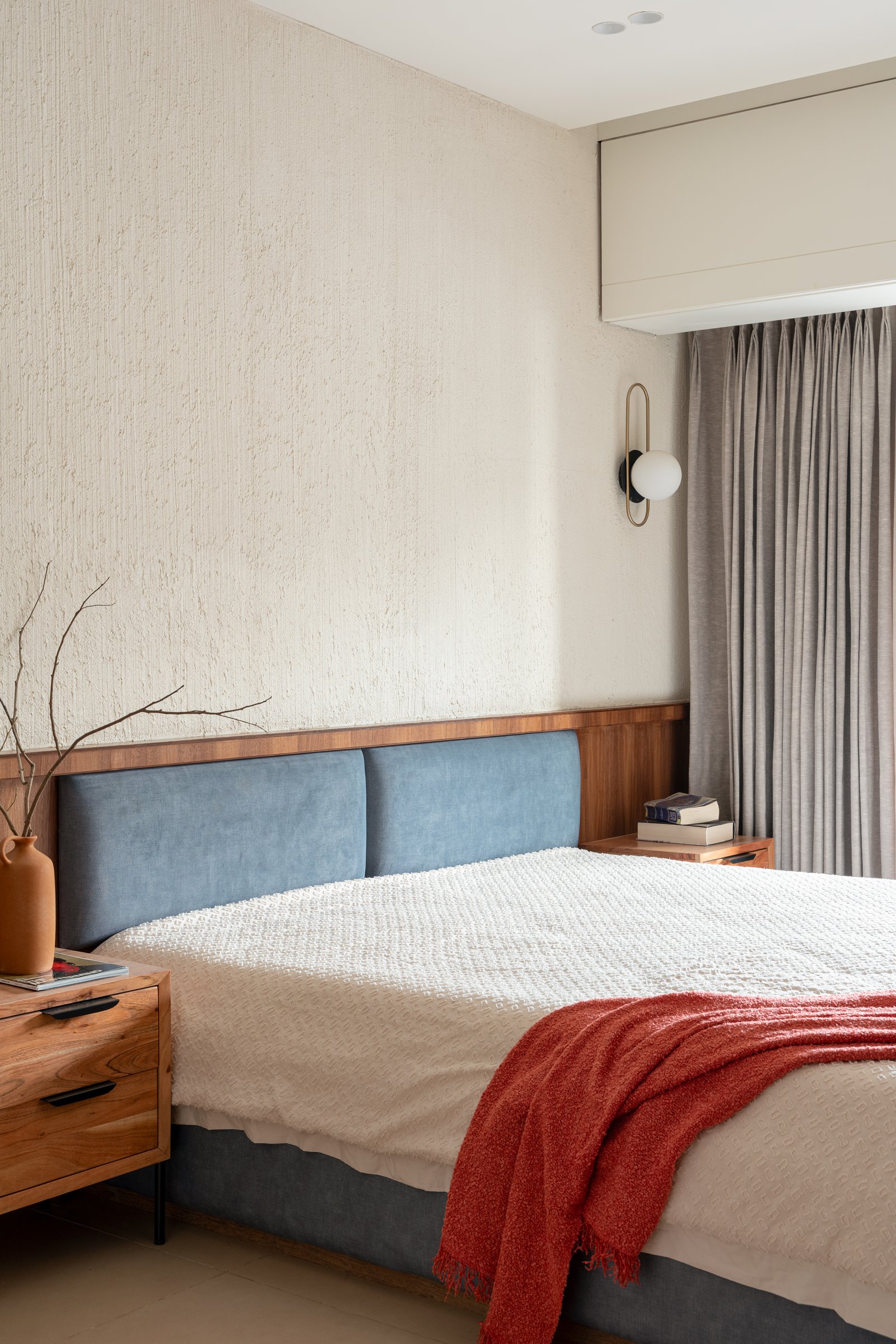 In the master bedroom, textured cream plaster meets a walnut wainscot and a soft blue upholstered headboard