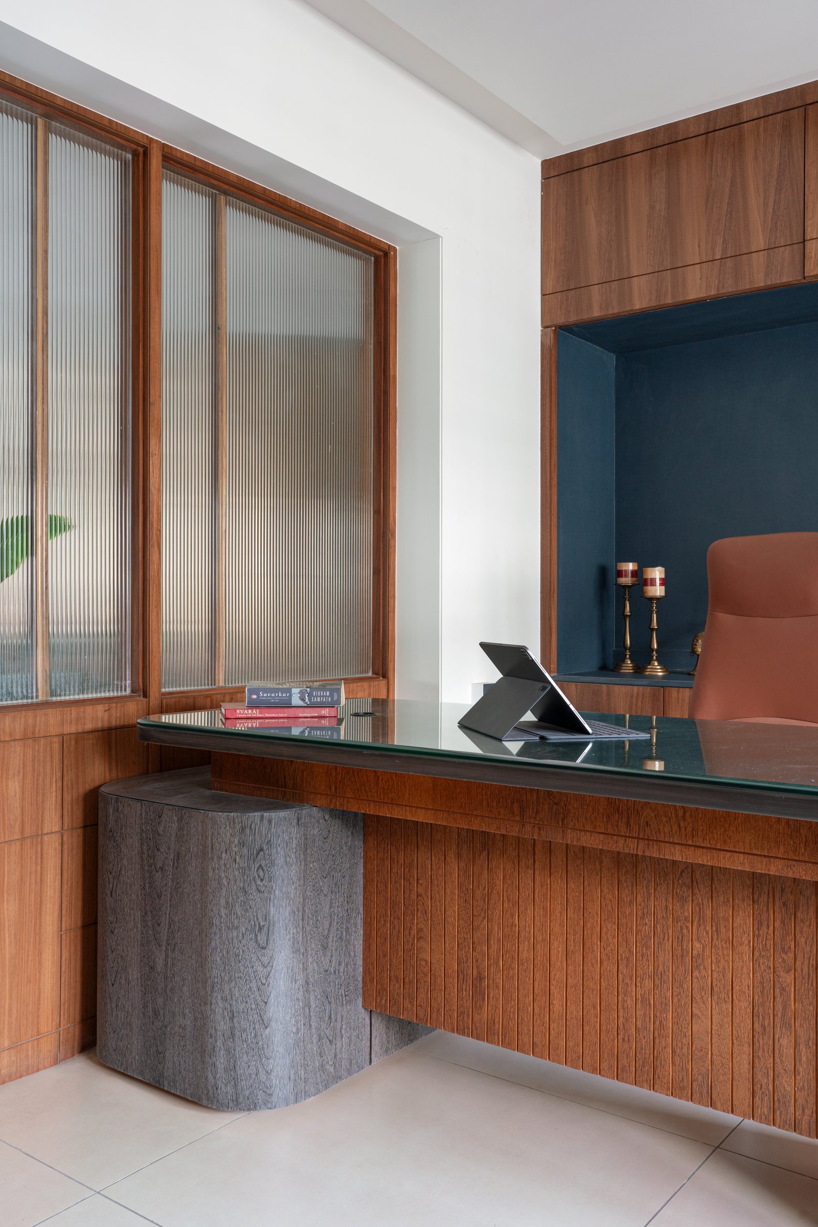The study, carved from the living room through fluted glass, holds a glass-topped desk and a deep teal reading niche