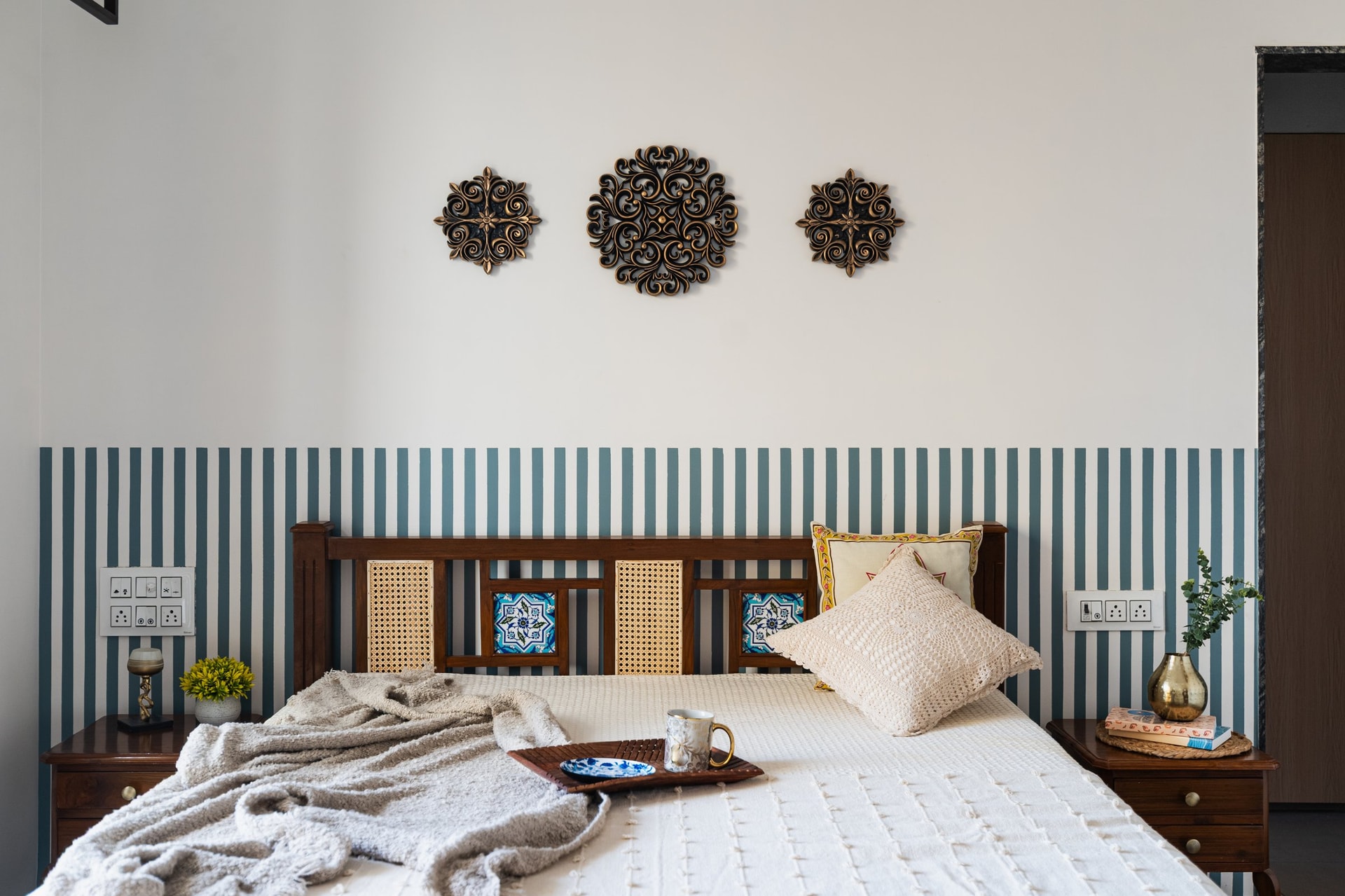 The master bedroom: a teal-and-white striped band, three carved metallic rosettes, and a headboard combining cane, turned wood and inset ceramic tiles