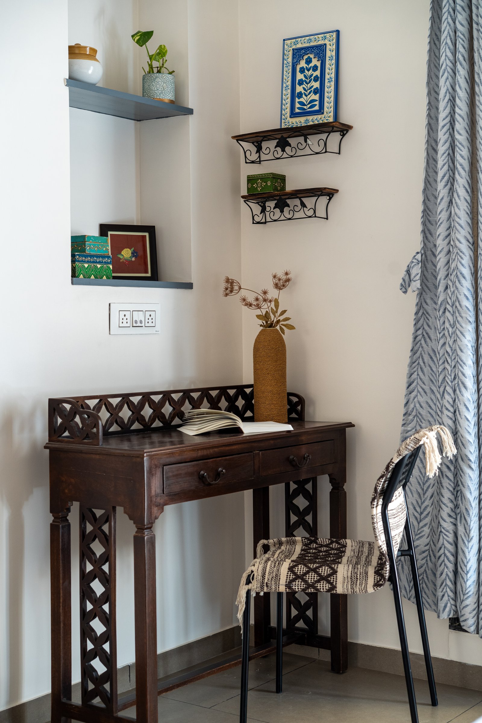 A study nook composed from a lattice-detailed dark wood desk and scrolled iron wall brackets