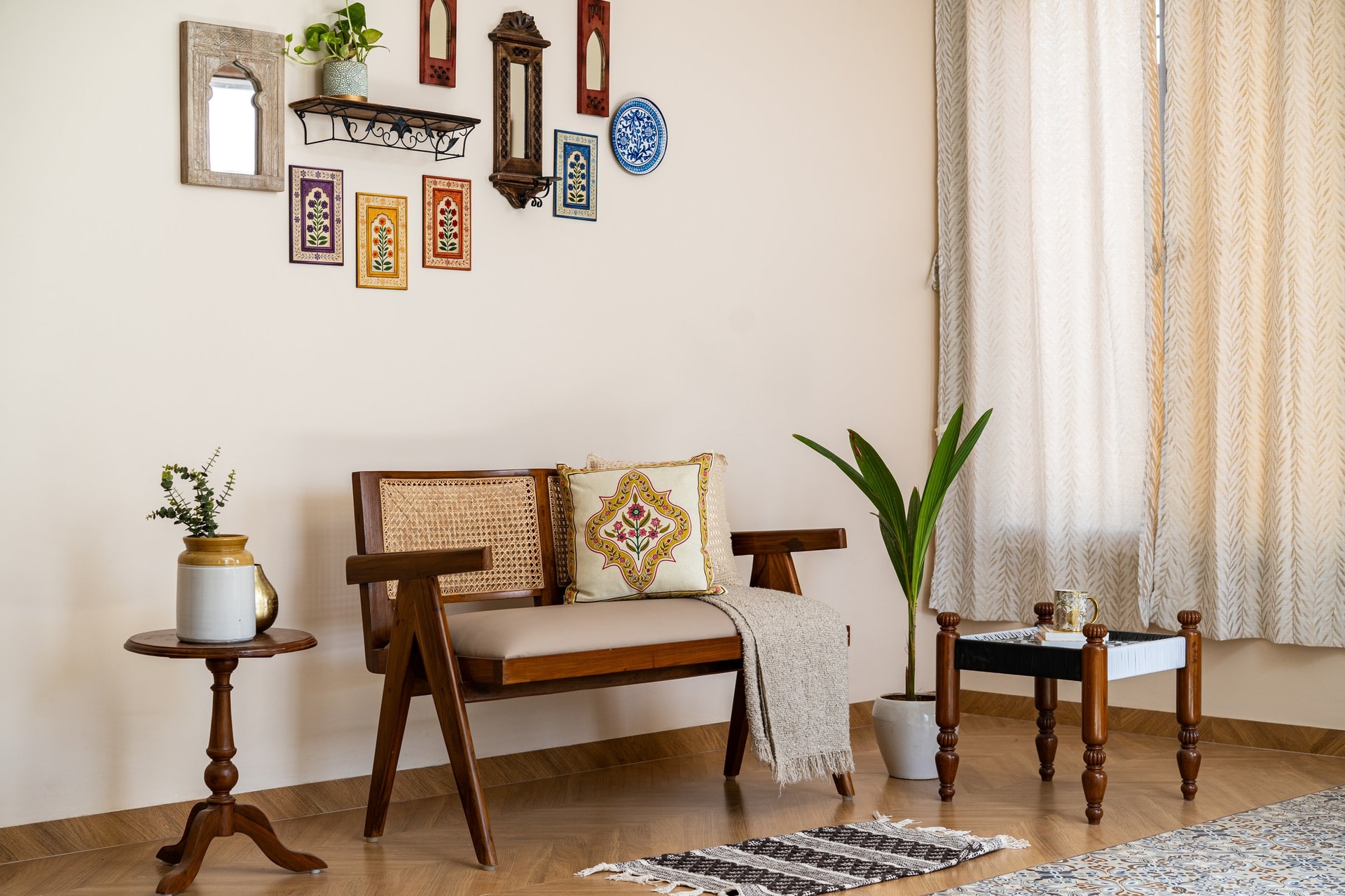 The upper living zone, a Chandigarh-language settee beneath a curated wall of carved mirrors and miniature paintings