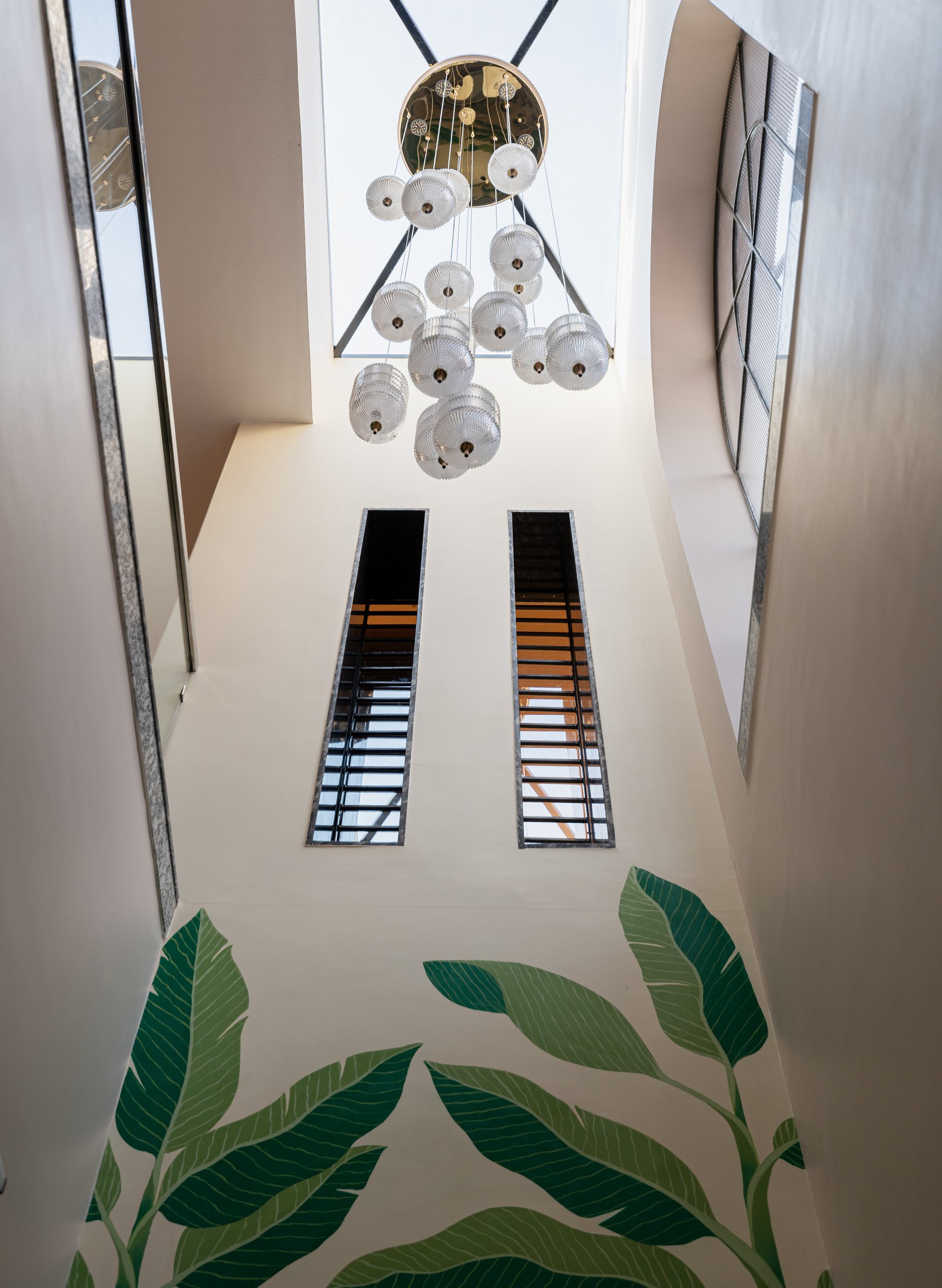 Looking up into the Chowk, where ribbed glass pendants descend from a brass rosette through the double-height volume