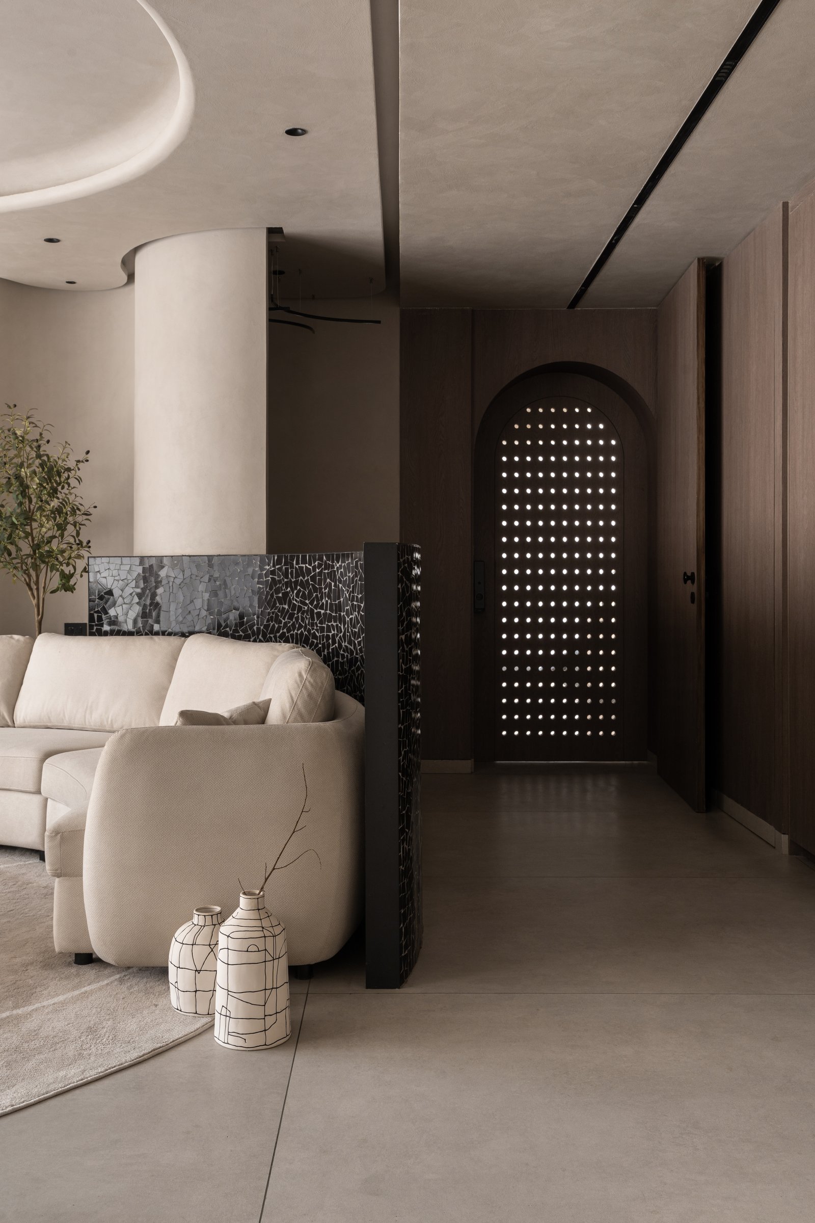 Seen from inside, the perforated door reads as a luminous screen, with the curved soffit and mosaic divider introducing the project's material vocabulary