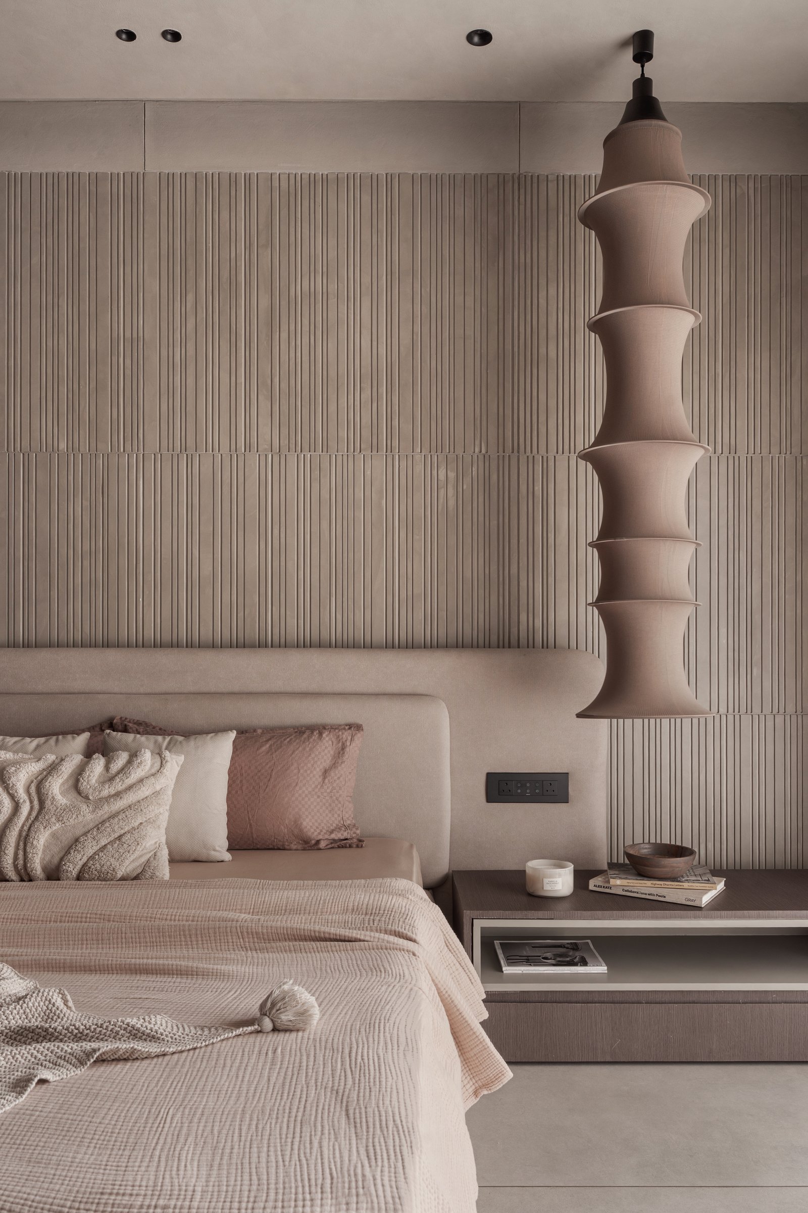 The tiered fabric pendant beside the bed, echoing the vertical reeding behind it