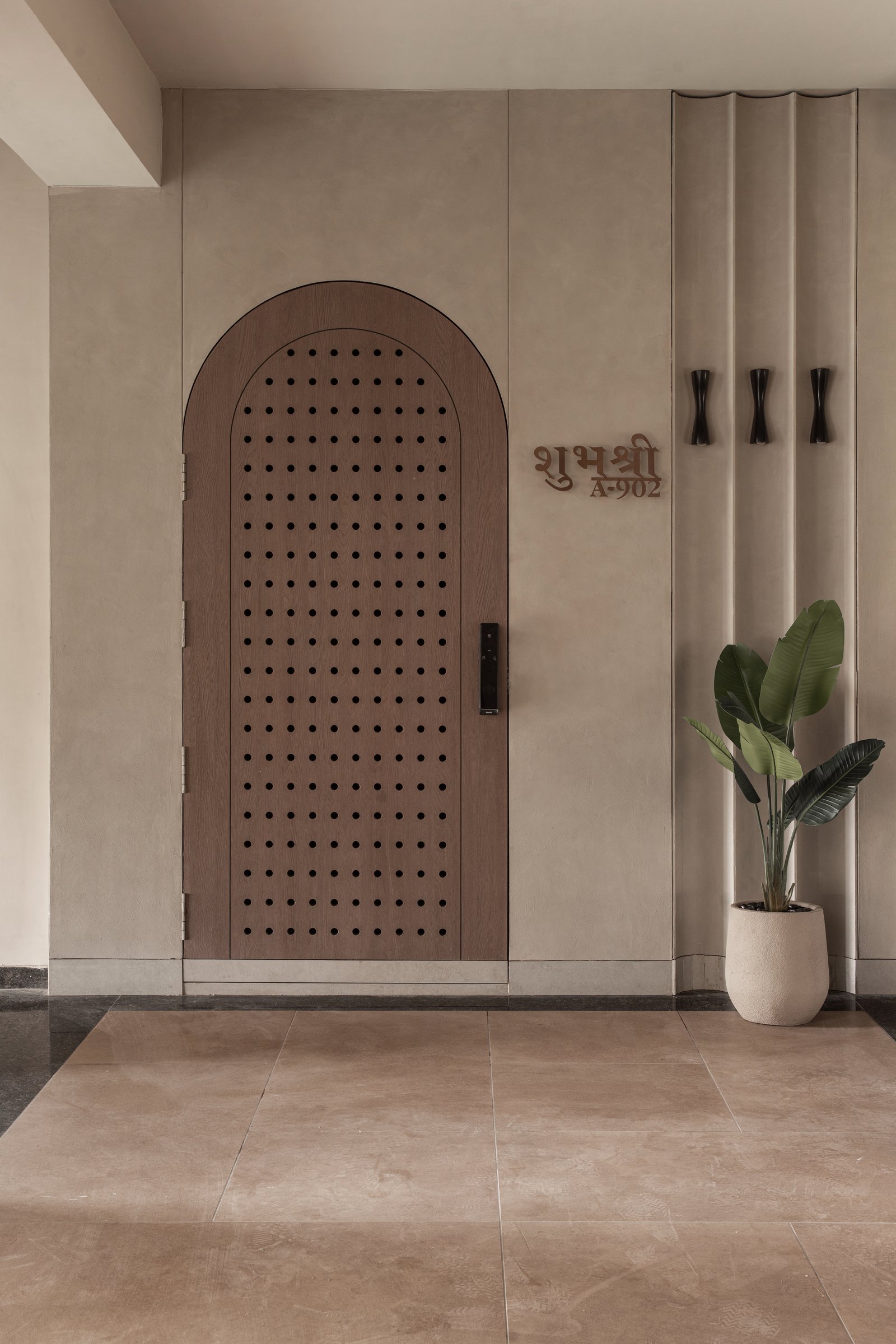 The entry: an arched, perforated wooden door set against fluted plaster establishes the home's central geometry before the apartment begins