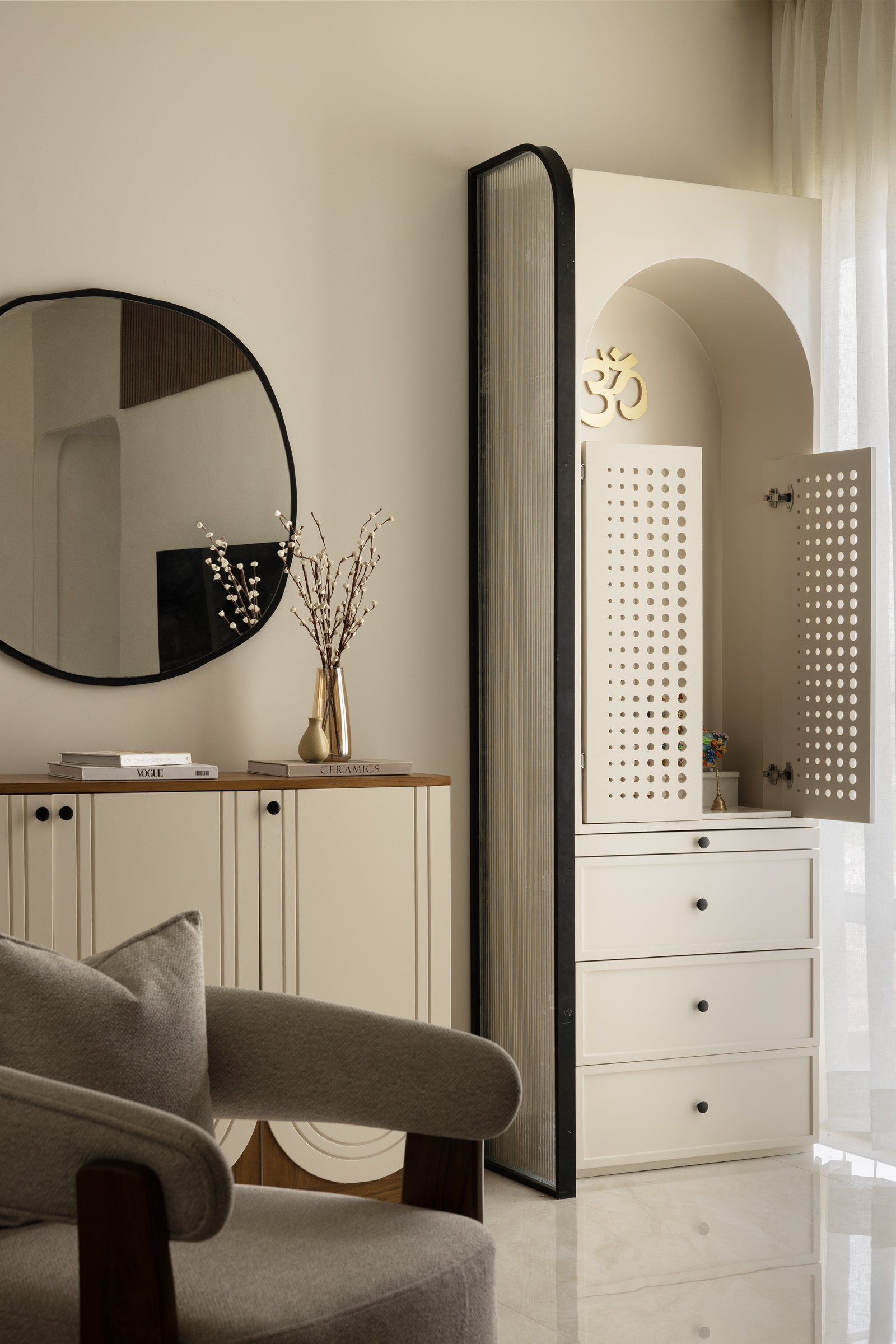 The foyer: a reeded sideboard, an organic mirror, and a fluted glass screen guarding the arched mandir niche beyond
