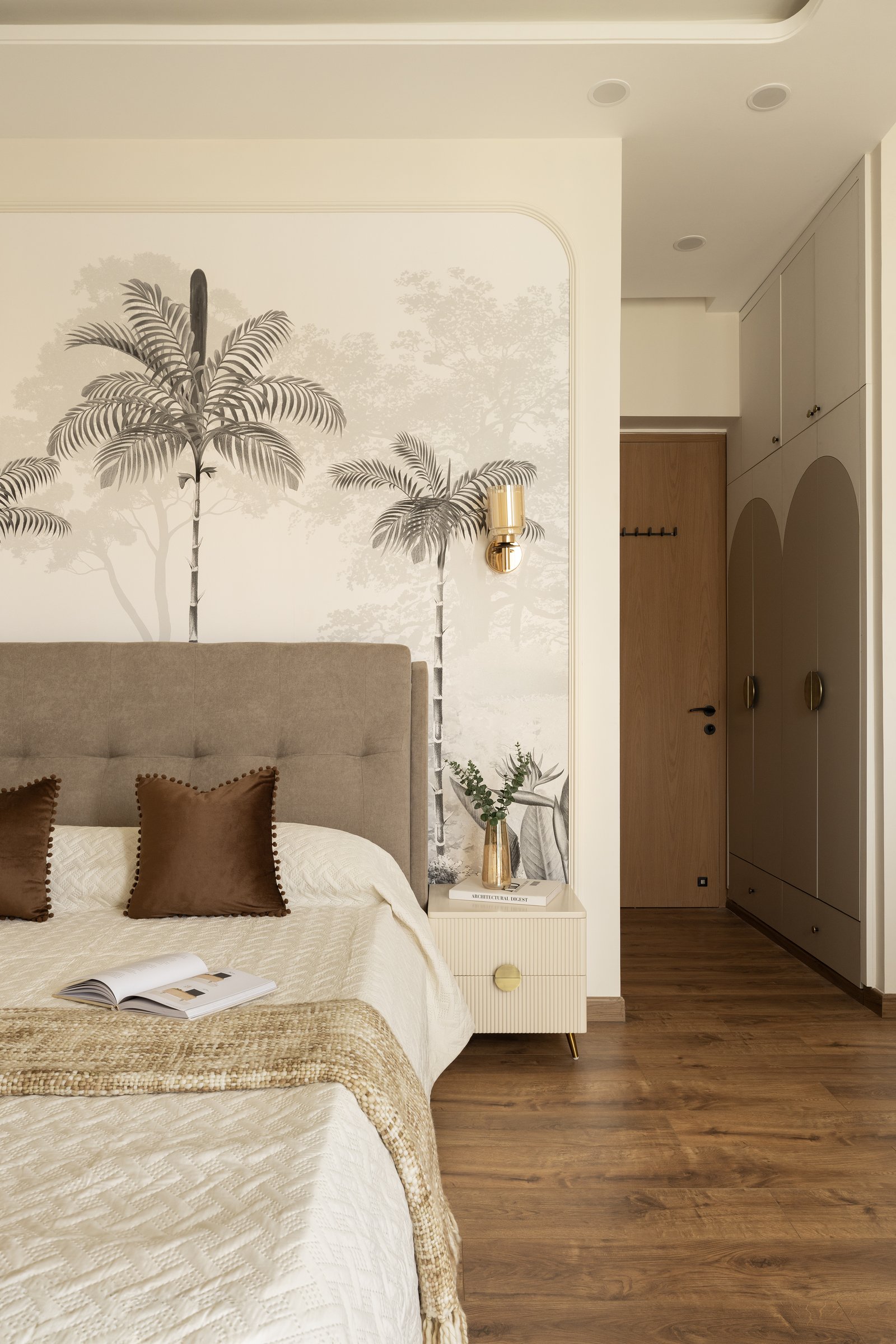 The master bedroom, where a sepia tropical mural sits beneath an arched panel and a disciplined wardrobe run