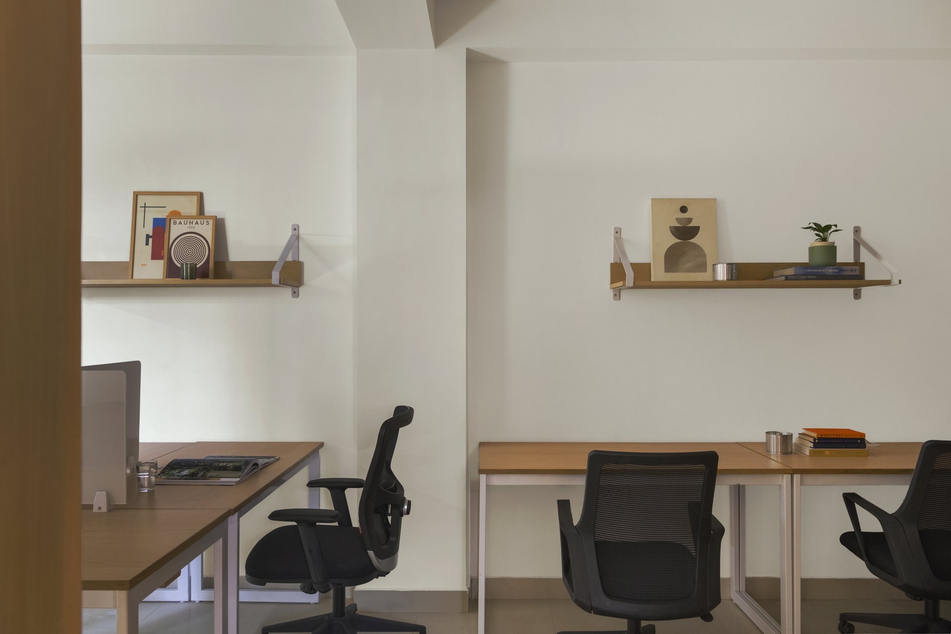 Paired desks backed by slim wood shelves, each carrying the same restrained vignette of print, ceramic, and book