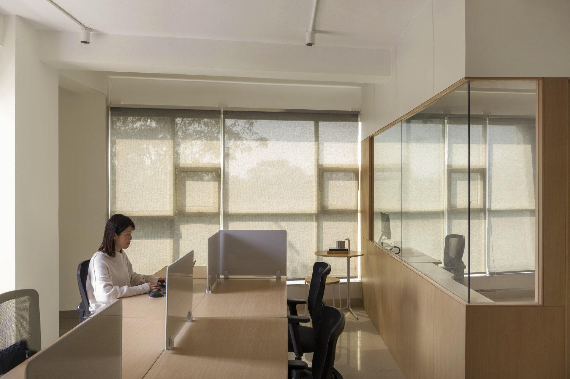 The main work hall, where sheer roller blinds turn the Delhi sun into a fabric-filtered wash across continuous birch desks
