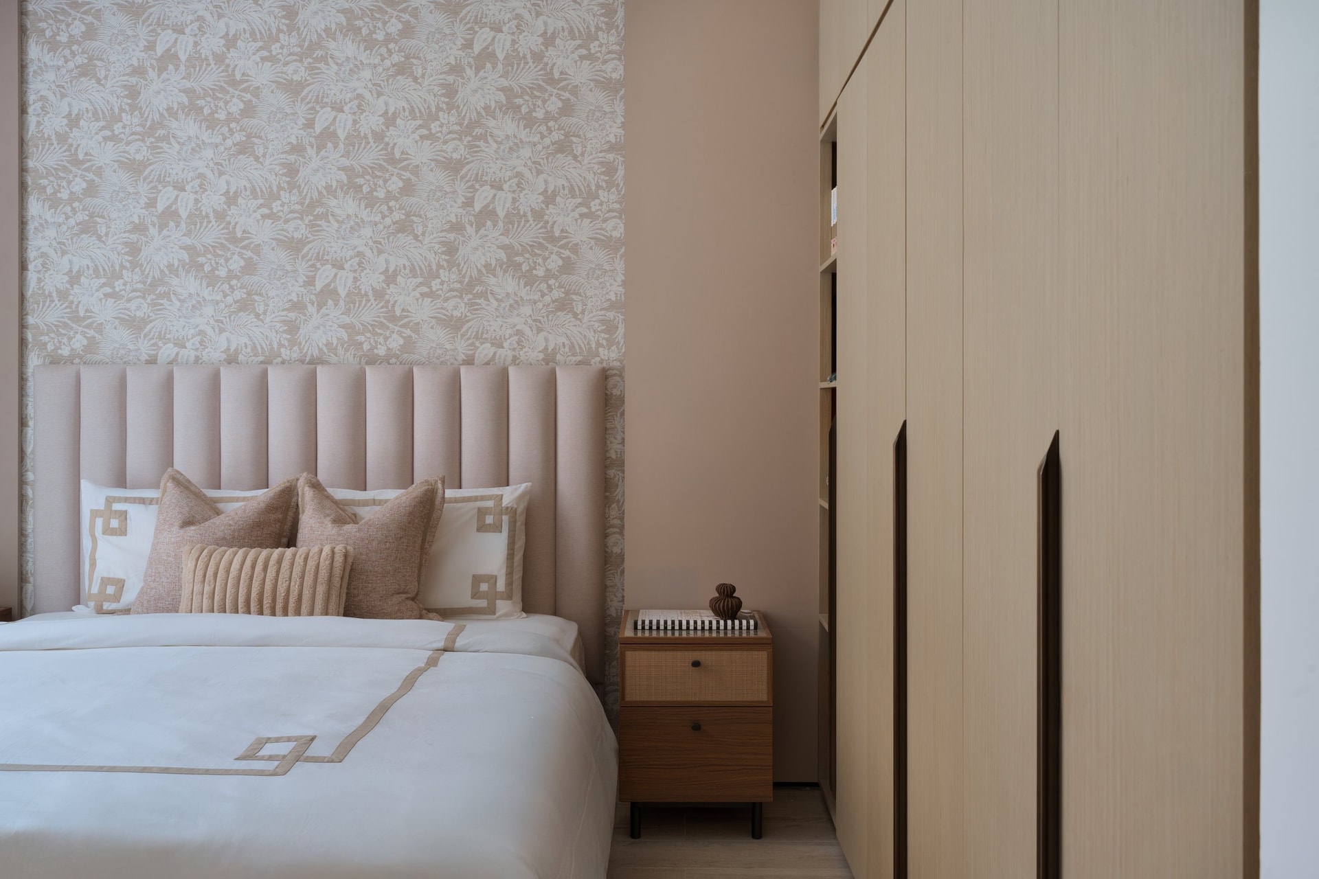 The second bedroom, where built-in oak wardrobes dissolve into the wall plane and leave the blush headboard to do the visual work