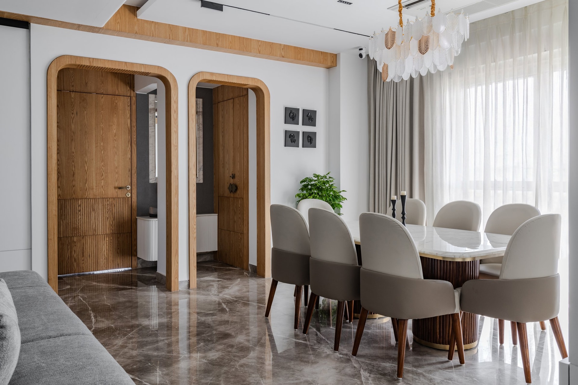 The dining area, anchored by a marble-topped table on a fluted wooden base and a layered shell-like chandelier