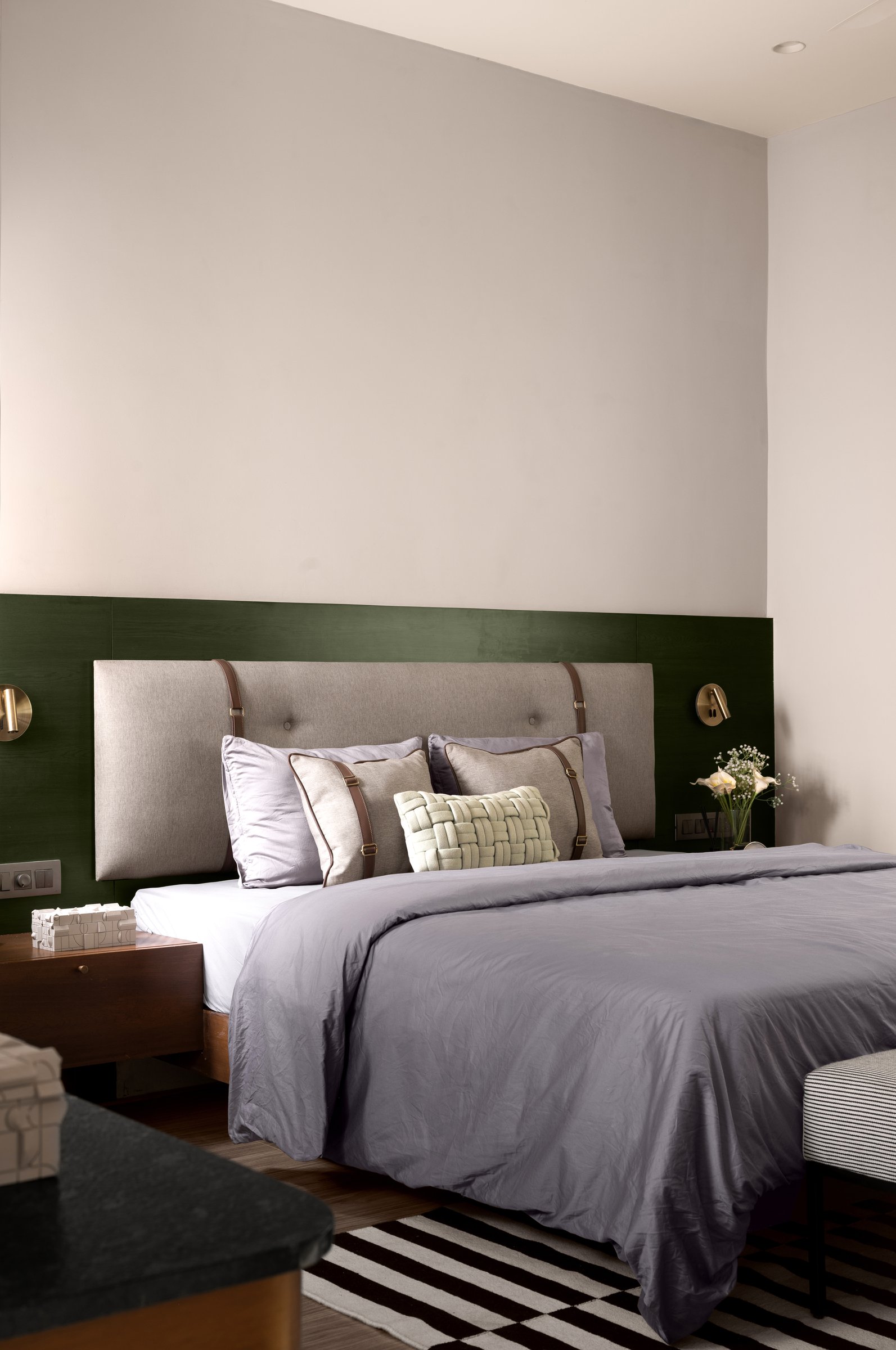 The primary bedroom, where a deep green band behind the headboard grounds the otherwise neutral envelope