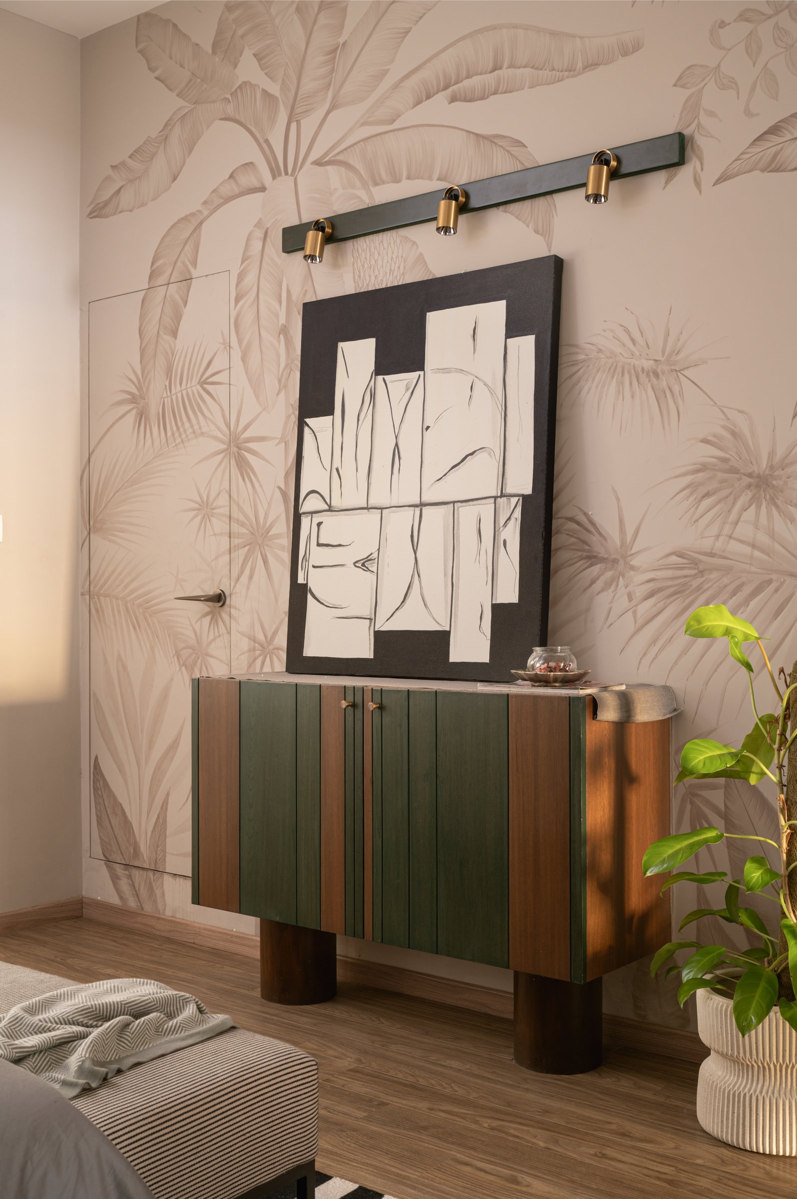 The bedroom's sideboard in panelled green and walnut, set against a wallpapered wall of muted palm fronds