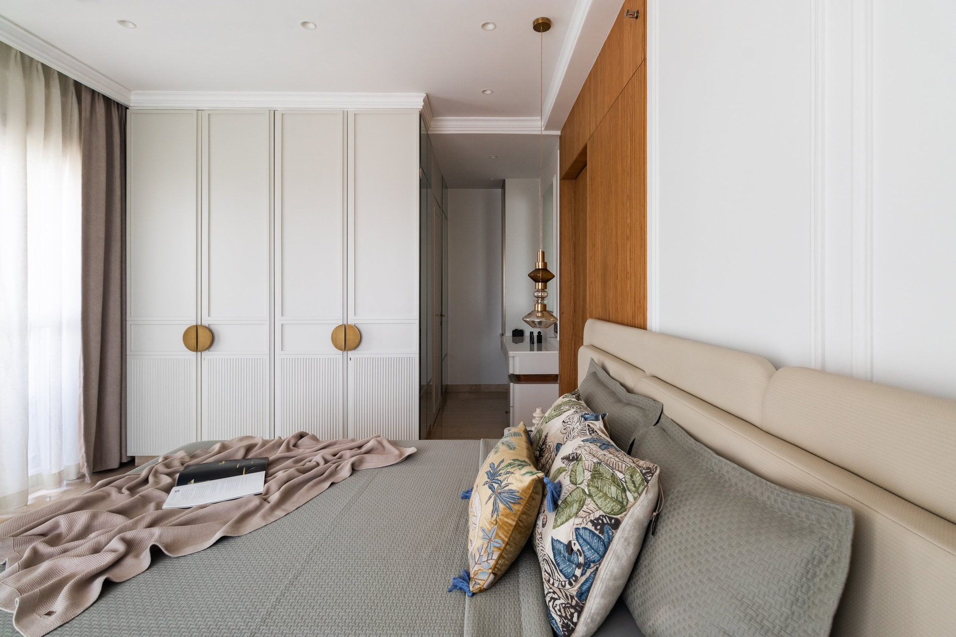 The dressing zone, defined by tall ivory wardrobes with circular brass pulls and fluted base panels