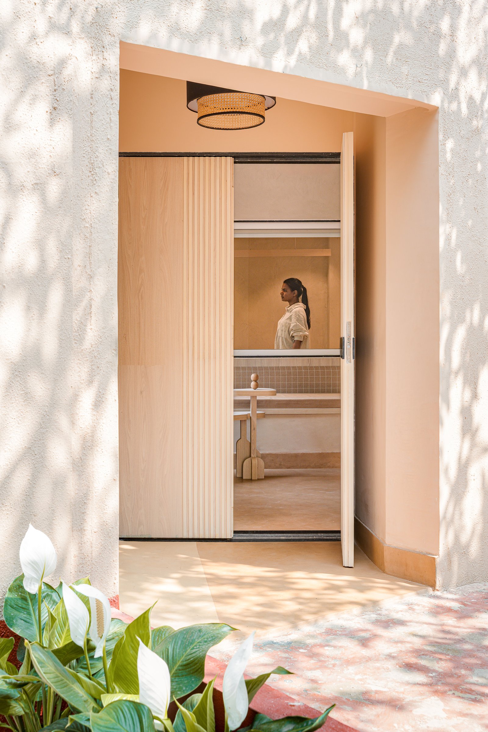 The entry porch, where a half-fluted pivoting door is dappled by the champa canopy above
