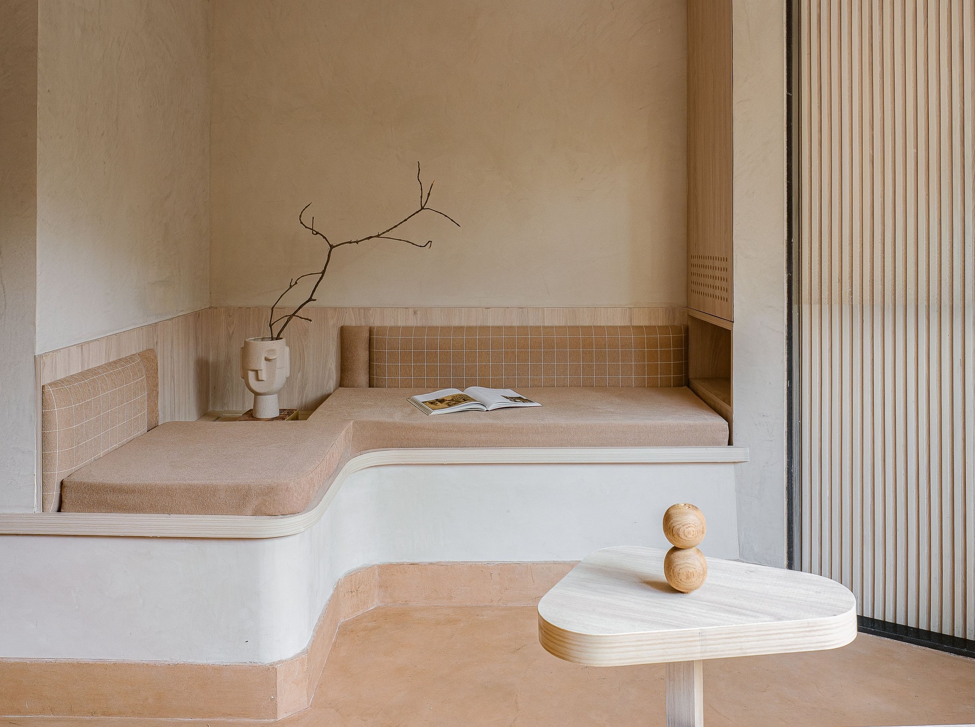 The L-shaped bench: warm sand upholstery on a terracotta-tinted oxide plinth