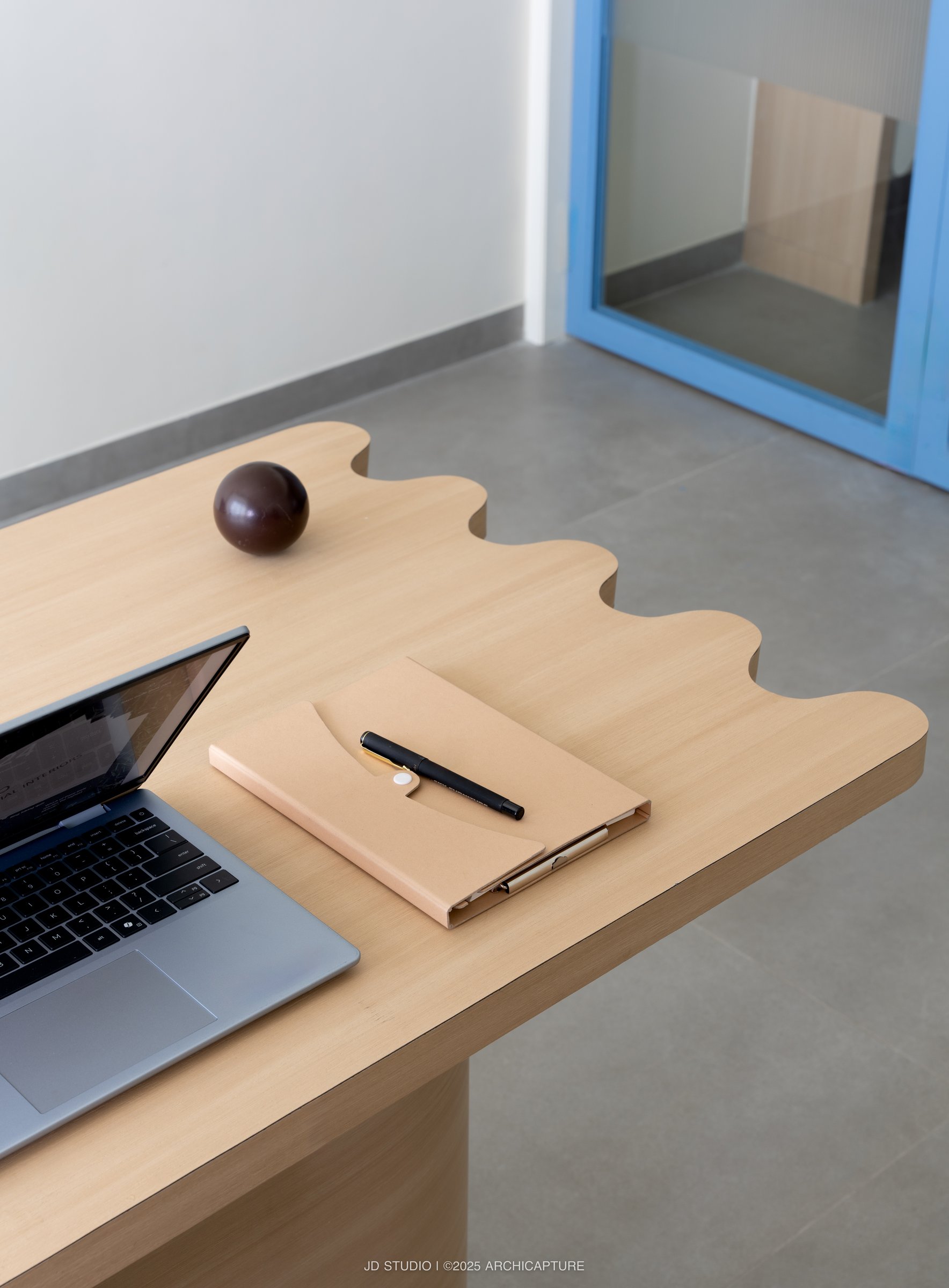 The scalloped oak desk edge in close-up, the project's formal idea reduced to a single profile