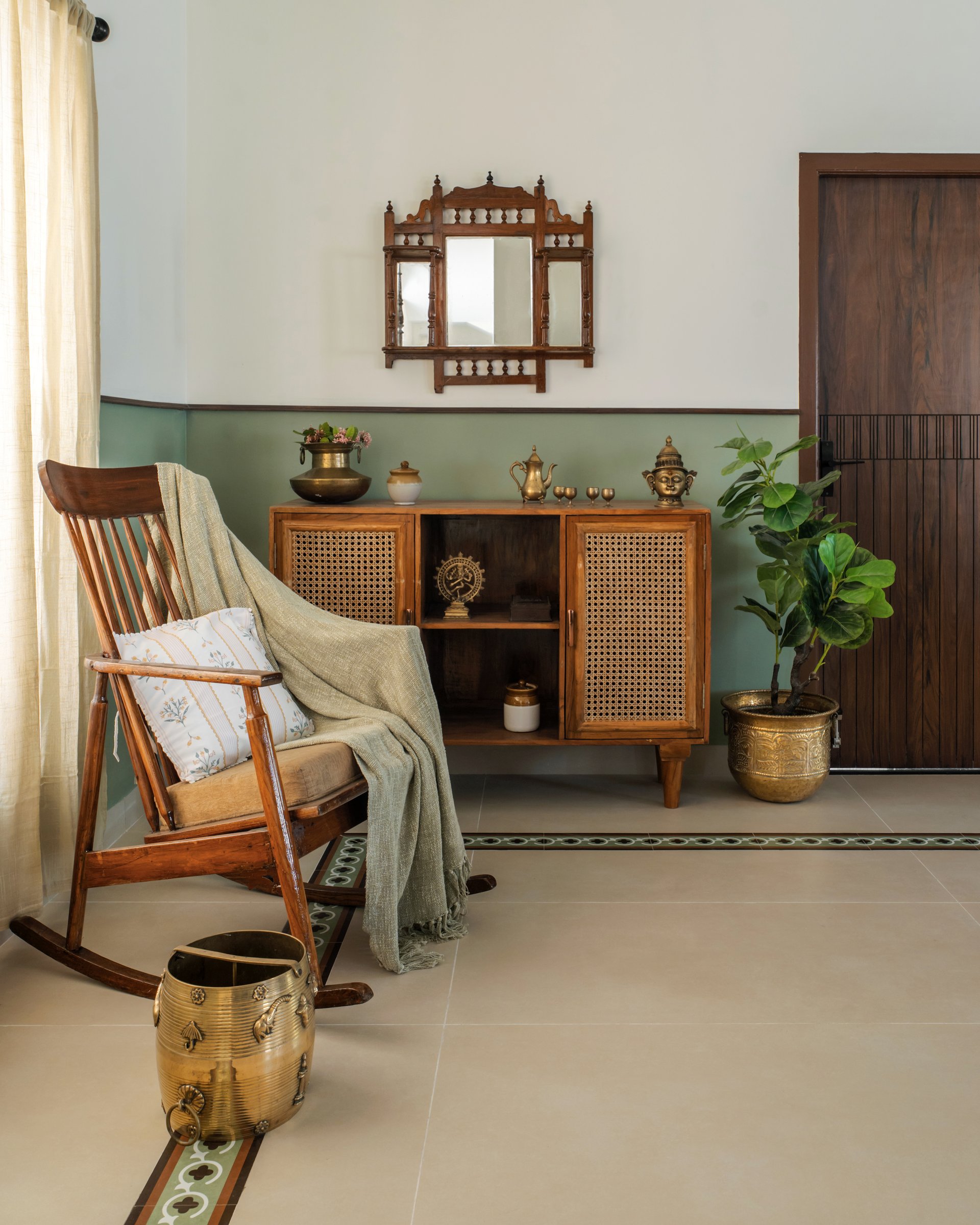 A vignette beside the entry: a rocking chair, a spindled mirror, and a caned sideboard set with brass vessels