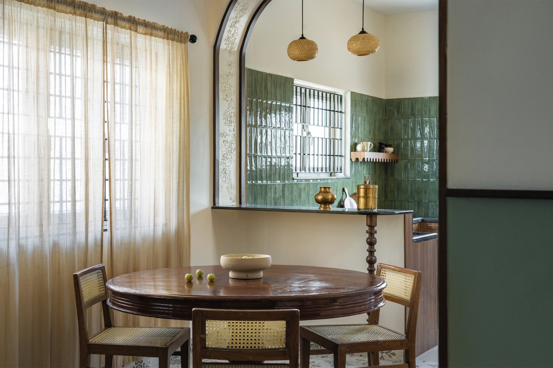 The dining table set in its own pocket of light beneath two woven rattan pendants, with a service ledge under the arched opening