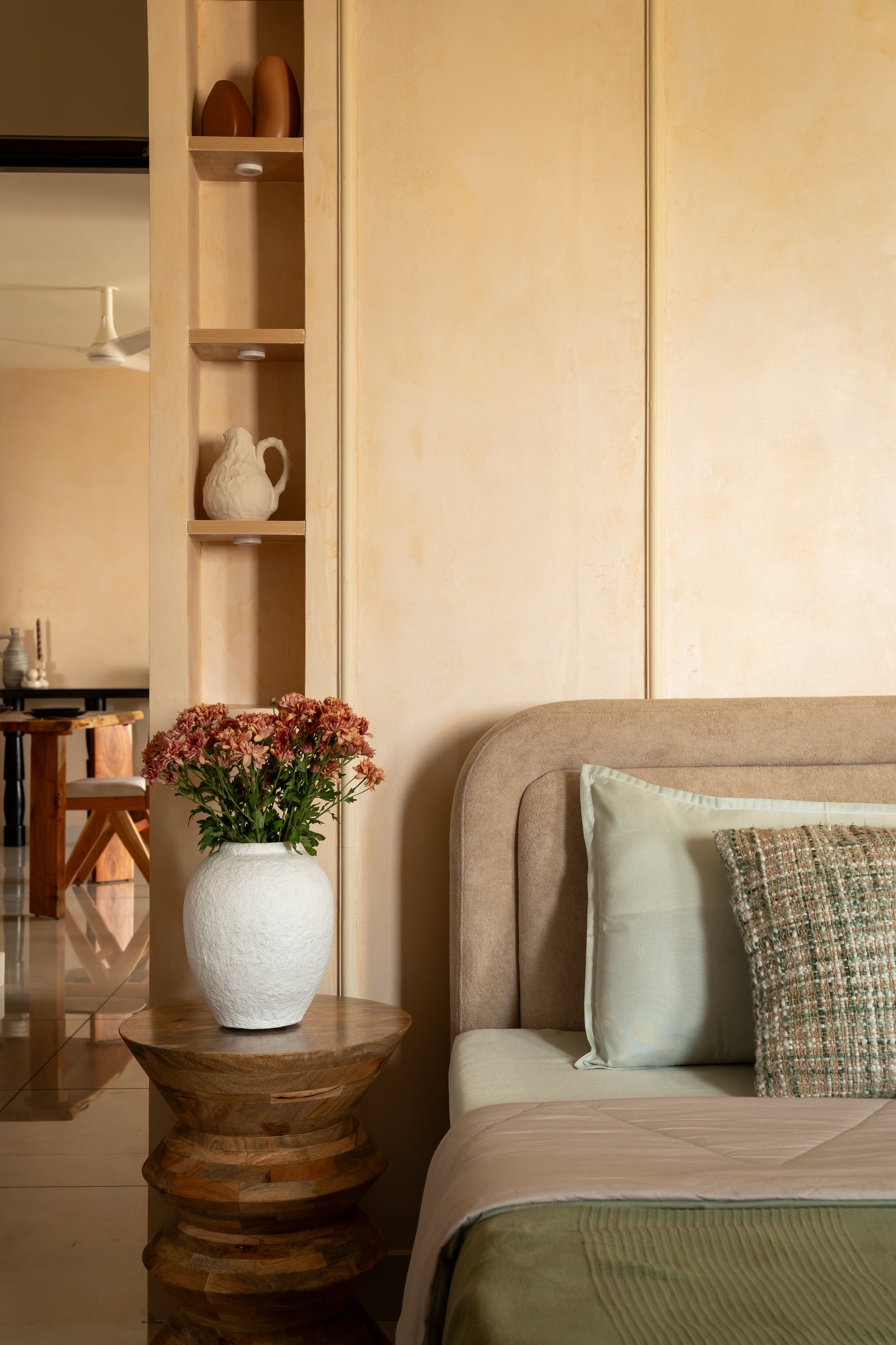 In the master bedroom, a lime-washed apricot wall and a slim built-in niche frame the curved suede headboard