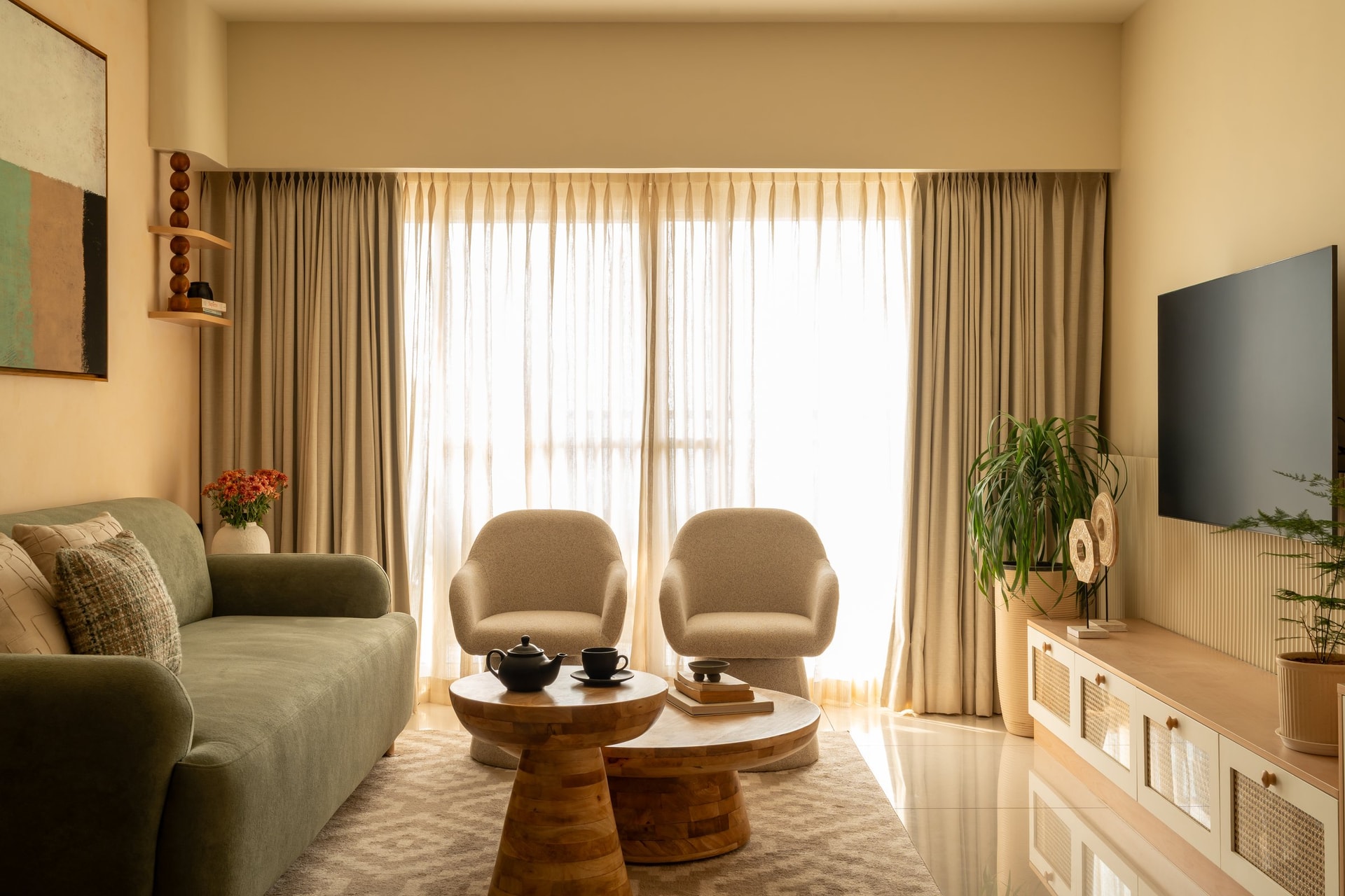 The living room, where sage upholstery, sheer drapery and rounded mango-wood tables hold the same tonal family as the walls