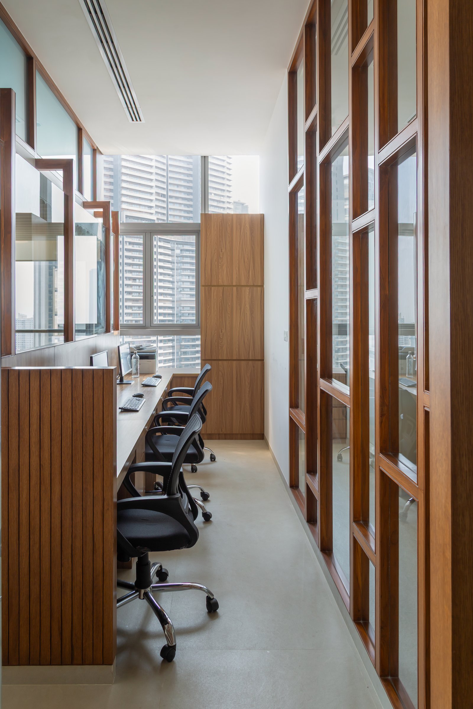 The narrow workstation corridor, where a continuous wood-fronted desk runs along a slatted screen and a tall cabinet anchors the far end