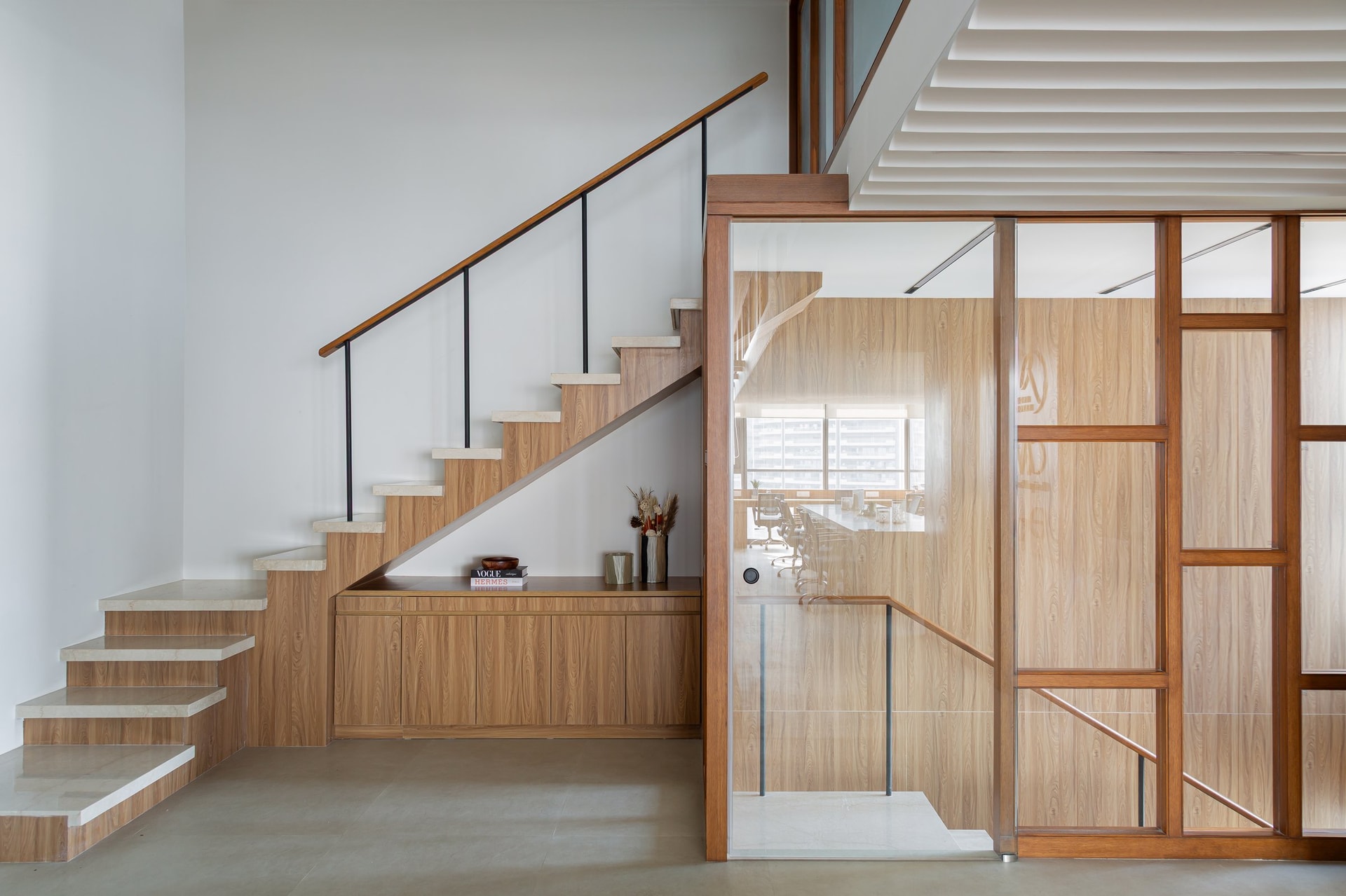 The cantilevered staircase, where stone treads, a wood-clad spine, and a slender metal balustrade with a wood-capped handrail negotiate the vertical link between floors