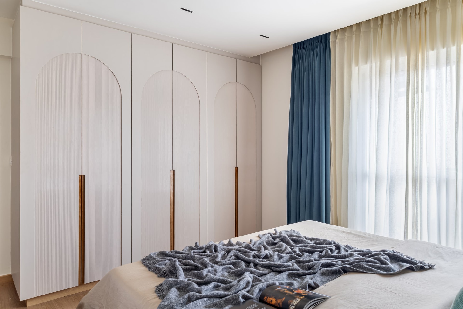 The wardrobe wall: three tall arched motifs routed into blush cabinet fronts echo curved thresholds elsewhere